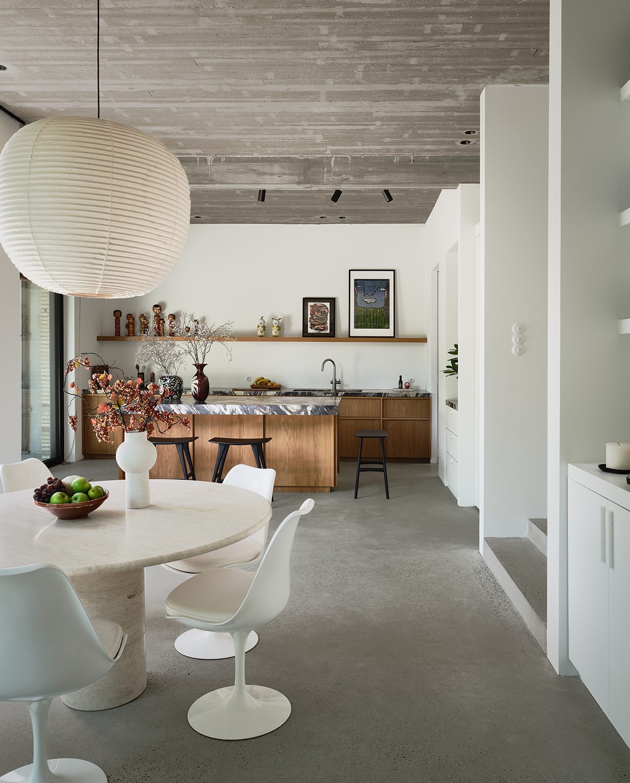 Boven de oude eettafel van Michelles oma hangt een handgemaakte lamp van Kojima Shoten, die haar ouders meenamen uit Japan. Tulip Chairs van Eero Saarinen. Krukken Ethnicraft. Op het schap staan Kokeshi dolls, een kunstwerk van Michelles moeder en een schilderij van Sylvain Serneels via Studio Borgerstein, een artistieke werkplek voor kunstenaars met een verstandelijke beperking. stijlvol wonen 2-2025 | fotografie Mr Frank | tekst Maya Toebat