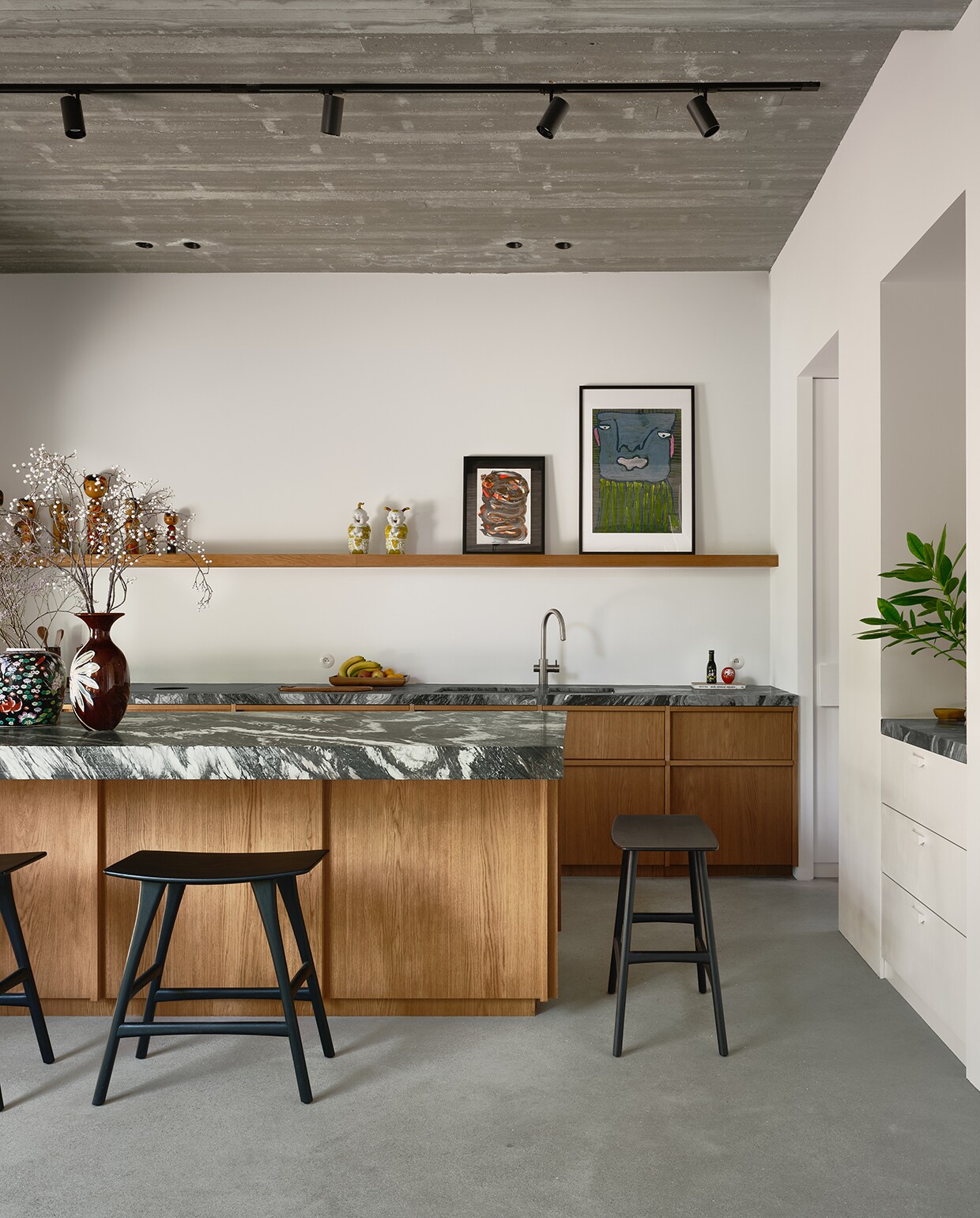 Michelle had een specifieke steen voor de keuken in gedachten, maar die was niet op voorraad. De steenhouwer ging in Italië op zoek naar nieuwe platen en op basis van foto’s koos ze voor de natuursteen Cipollino, gecombineerd met eikenfineer. Krukken Ethnicraft. Op de plank Kokeshi dolls, een kunstwerk van Michelles moeder en een schilderij van Sylvain Serneels via Studio Borgerstein. stijlvol wonen 2-2025 | fotografie Mr Frank | tekst Maya Toebat