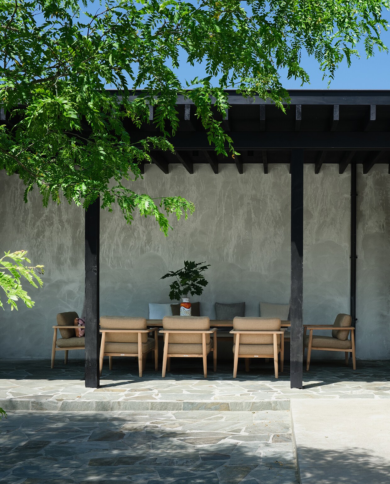 Tafel en stoelen onder overkapping Royal Botania. Op de patio trekt een beige stoel uit teak en touw de aandacht. Het gaat om een prototype van de Futo Maki Chair, een uniek ontwerp van Michelle, dat exclusief verkrijgbaar is bij ’t Huis van Oordeghem als onderdeel van de Okinawa Objects collectie. stijlvol wonen 2-2025 | fotografie Mr Frank | tekst Maya Toebat