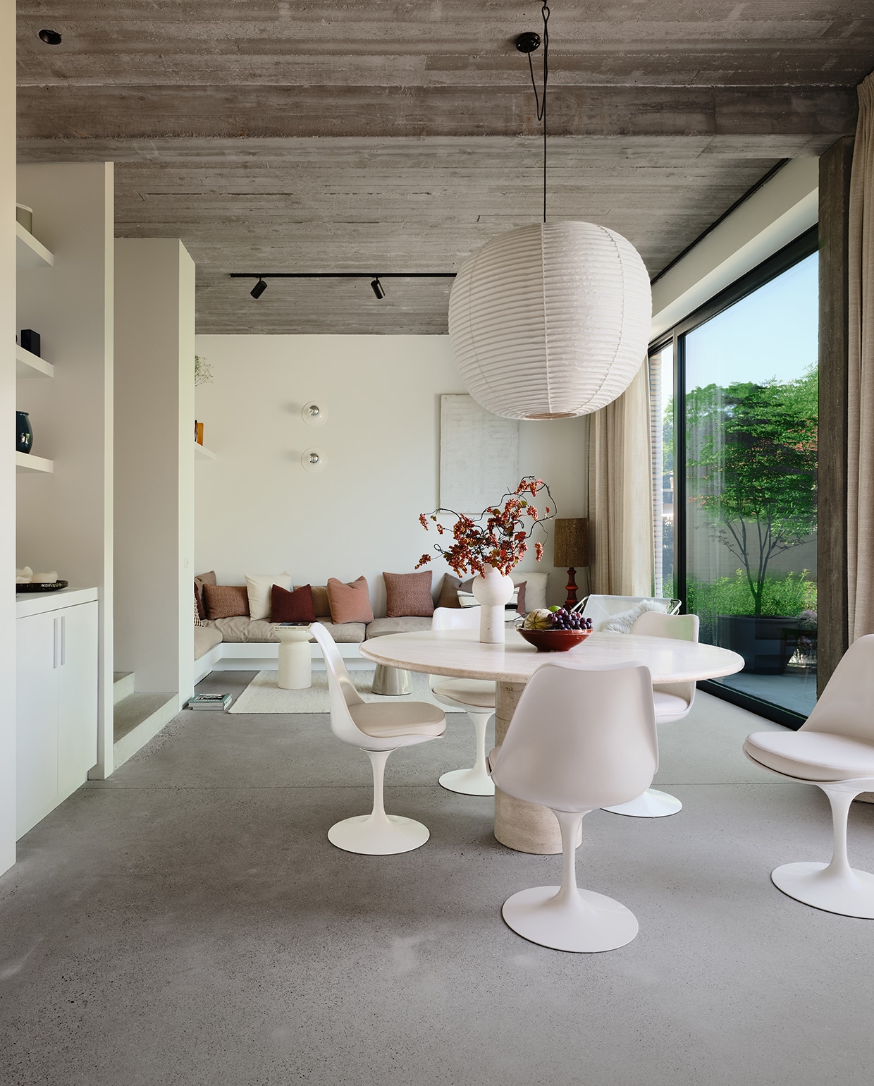 De zithoek met ingebouwde bank nodigt uit om te borrelen met vrienden. De linnen gordijnen geven warmte aan de ruimte, de grote ramen betrekken de tuin bij het huis. Eettafel van Michelles oma, handgemaakte lamp van Kojima Shoten uit Japan. Tulip Chairs van Eero Saarinen. Wandlampen Zangra, witte kunstwerk uit beton Jef Meyer. stijlvol wonen 2-2025 | fotografie Mr Frank | tekst Maya Toebat