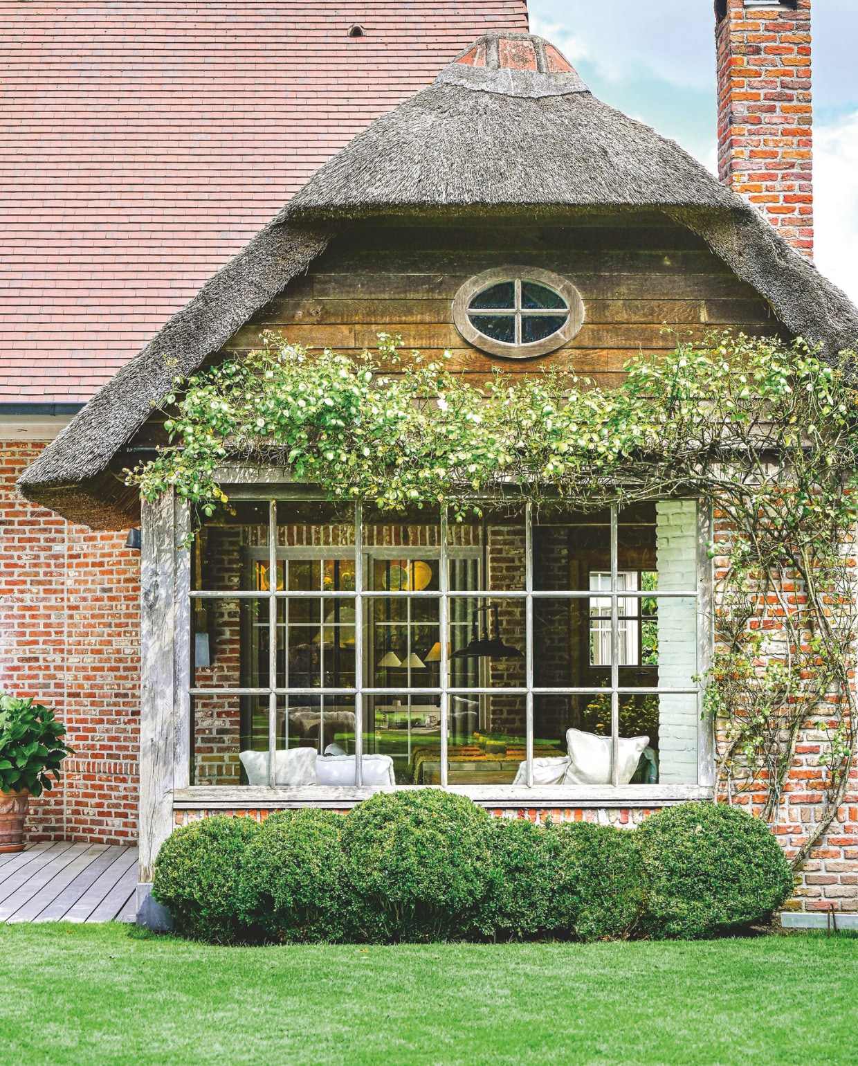 Onder het raam van het overdekte terras staan bollen buxus. Tegen de muur een klimroos. vtwonen Landelijk 2-2025 | Fotografie Claude Smekens | Tekst Yvonne van Galen