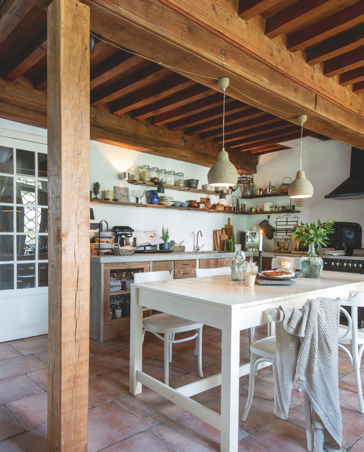 De eettafel stond al in het huis.  Witte caféstoelen Oud is Nieuw. Een combinatie van wandspots en hanglampen zorgt voor gezellig licht. vtwonen Landelijk 2-2025 | styling Peet Styling! | fotografie Joyce Vloet | tekst Marie Masureel