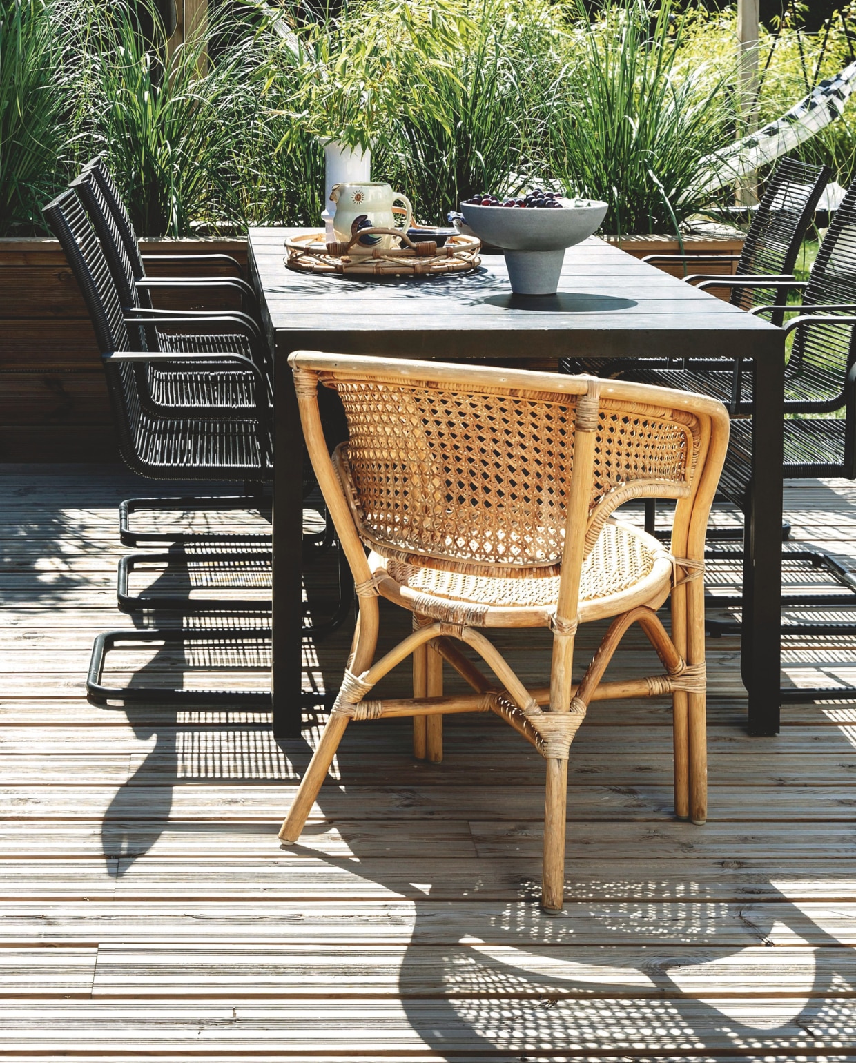 De eettafel van Sylvan wordt afgeschermd door een hoge plantenbak met pampasgras (Cortadera selloana). Zwarte stoelen Ikea. Rieten stoel tweedehands. Dienblad Ikea, keramiek van de vlooienmarkt. Schaal 101 Copenhagen. vtwonen tuin 11| productie living inside | styling en tekst rikke graff juel | fotografie christina kayser o. | tekst ina babbé