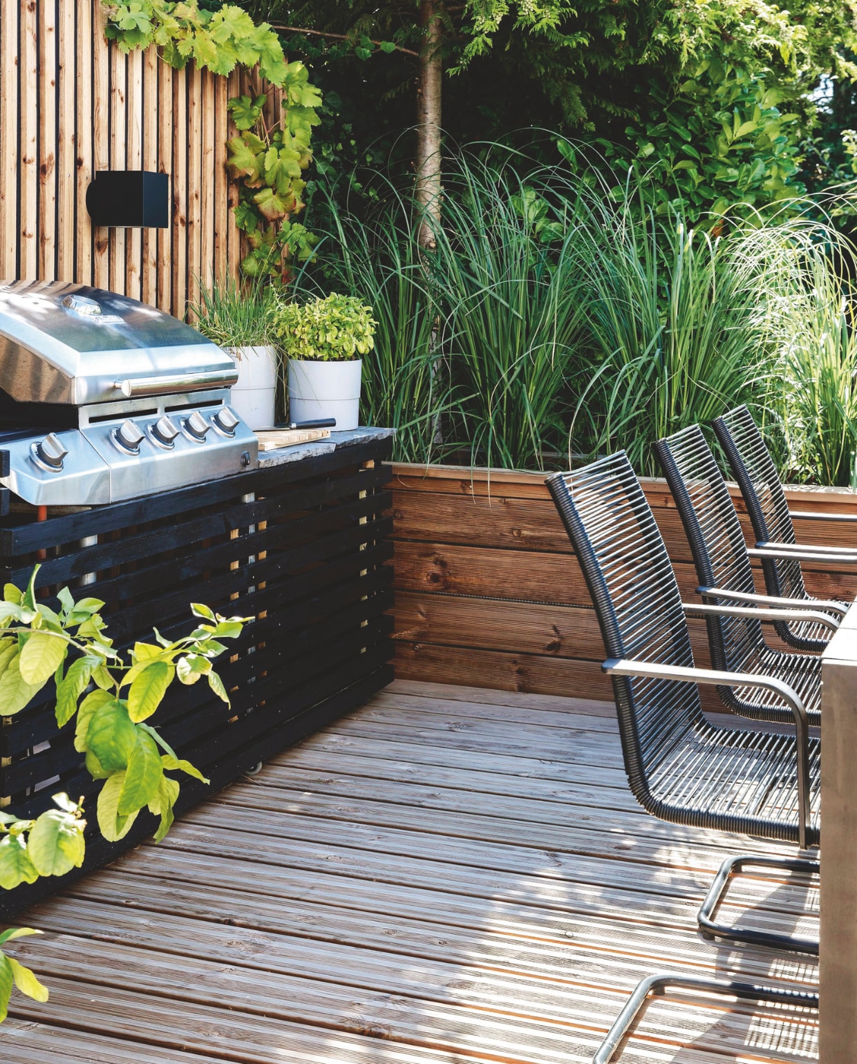 De barbecue is omtimmerd met zwartgebeitst hout. Ernaast is afzetruimte gecreëerd met een marmeren plaat. Daarop kruidenpotten met basilicum en bieslook. Over de schutting kruipt een druif (Vitis). Soortgelijke barbecue Boretti. vtwonen tuin 11 | productie living inside | styling en tekst rikke graff juel | fotografie christina kayser o. | tekst ina babbé