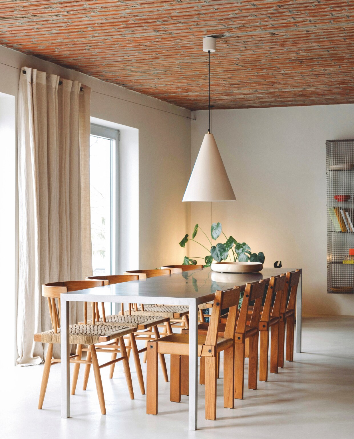 Geraldine speelt graag met contrasten door een maatwerk metalen tafel te combineren met twee reeksen vintage stoelen van Pierre Chapo en George Nakashima. Stijlvol Wonen 03-2025 | Fotografie Stie De Neve | Tekst Maya Toebat