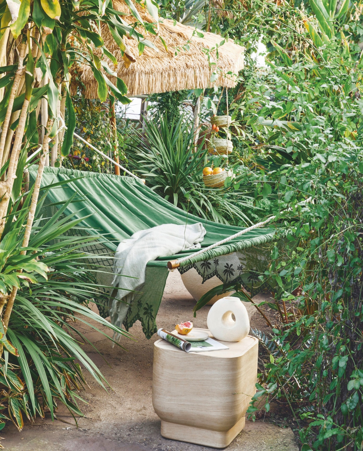 Katoenen hangmat Olive, 115x210 cm (bxl) € 499,-, parasol Patio, raffia en aluminium, 300 cm (Ø) € 499,- (hkliving.com). Plaid, acryl, polyester en wol € 29,99 (hm.com). Keramieken vaas Spada Sand van Urban Nature Culture € 49,95, walnoothouten bord van Household Hardware € 14,99, zeegras etagère Essaouira, 70 cm (h) € 45,-, betonnen bijzettafel Noble van Zuiver, 45x45x47 cm (bxdxh)€ 469,- (shop.vtwonen.nl)  vtwonen 03-2025 | styling Kelly van Gendt | fotografie Peggy Janssen