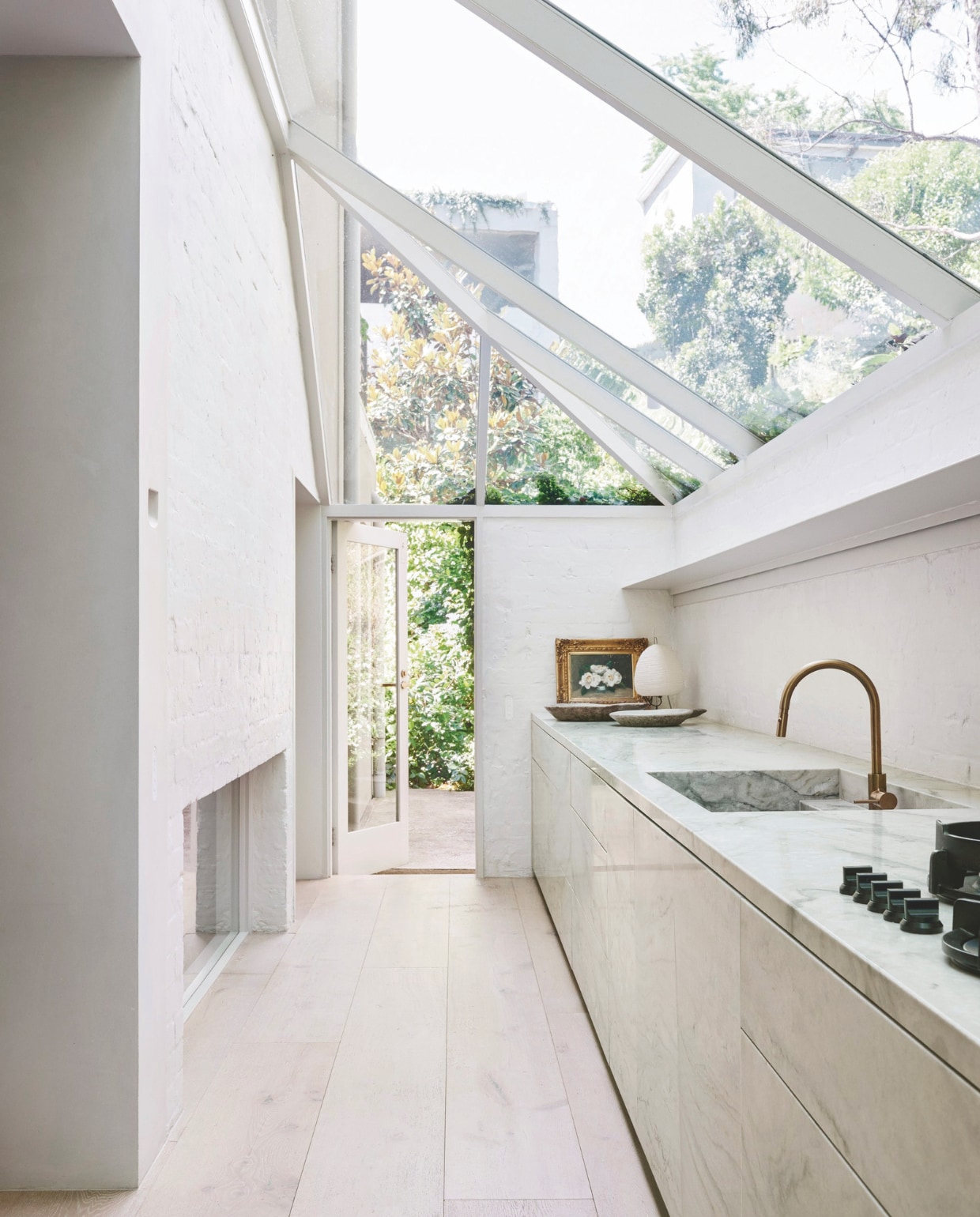 De minimalistische keuken is gemaakt van massief graniet. Tafellamp Akari is een ontwerp van Isamu Noguchi uit 1951. Schilderij gemaakt door Leonard Joel. vtwonen stijlvol 03-2025 | fotografie Lisa Cohen | tekst Tanne Donjacour Gielen | productie Living agency