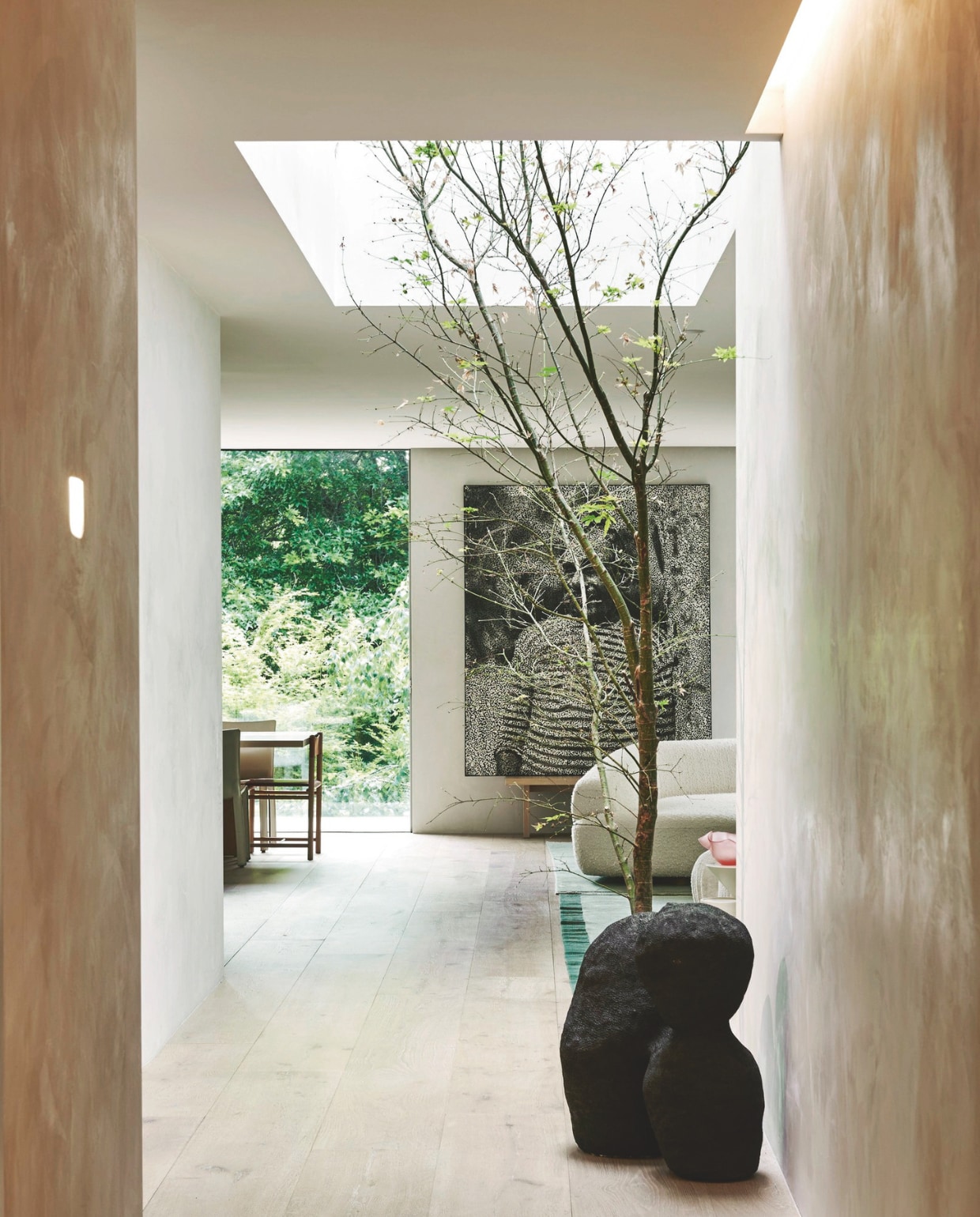 De gang die naar de living leidt, omarmt een boom die de natuur binnenhaalt. Stenen sculptuur van de jonge kunstenaar Isadora Vaughan. vtwonen stijlvol 03-2025 | fotografie Lisa Cohen | tekst Tanne Donjacour Gielen | productie Living agency