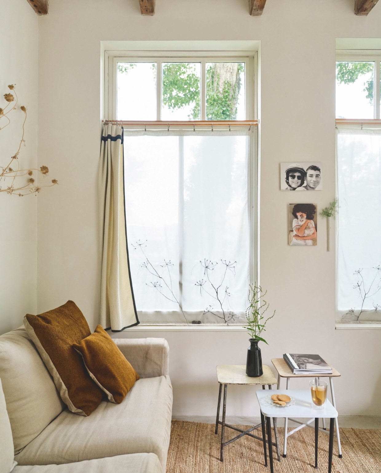Bank kringloop, bekleed met linnen. Kussens paardenhaar/linnen, gordijnen van kaasdoek met geborduurde schermbloemen, overgordijnen Brigit Vermeulen. Bijzettafels kringloop en Van Dijk & Ko. Vloerkleed Ikea. Vaas cadeau gekregen. Aan de muur familiefoto’s. Wandvaas Kastanje van Anneke Bruin. vtwonen 03-2025 | fotografie René van der Hulst