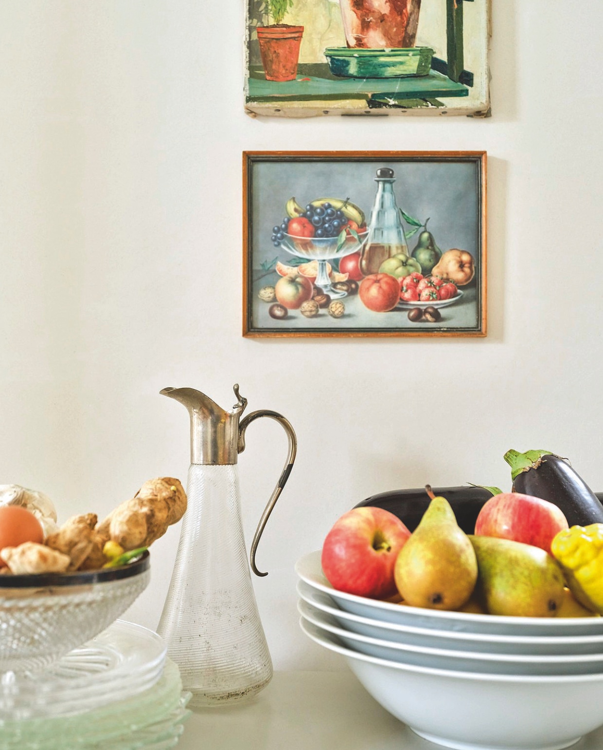 Stalen keukentrolley uit Tsjechië via Van Dijk & Ko, zelf geschilderd. De schilderijtjes komen van een garagesale en een kringloop. Witte schalen van een Italiaans hotelservies, glazen borden en schenkkan van moeder geërfd, glazen schaal met zilveren rand kringloop. vtwonen 03-2025 | fotografie René van der Hulst