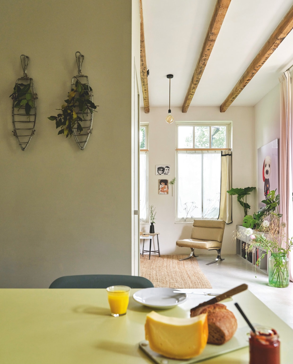 Muurkleur Portland Stone Dark van Little Greene. Kruidenrekken gemaakt van oude visroosters voor de barbecue. Tafelblad van de bouwmarkt op schragen van Hay, geverfd in Cornflower Field van Flexa Creations. Vloer gevlinderd beton. Bijzettafels Van Dijk & Ko en kringloop. Vloerkleed en wandmeubel Ikea. Aan de muur familiefoto’s. Wandvaas Kastanje van Anneke Bruin. Gordijnen van kaasdoek met geborduurde schermbloemen, overgordijnen en lamp Brigit Vermeulen. Fauteuil Zo Goed als Oud. Kunstwerk The Indispensable van Ilse Vermeulen. Glazen vaas Van Dijk & Ko. vtwonen 03-2025 | fotografie René van der Hulst