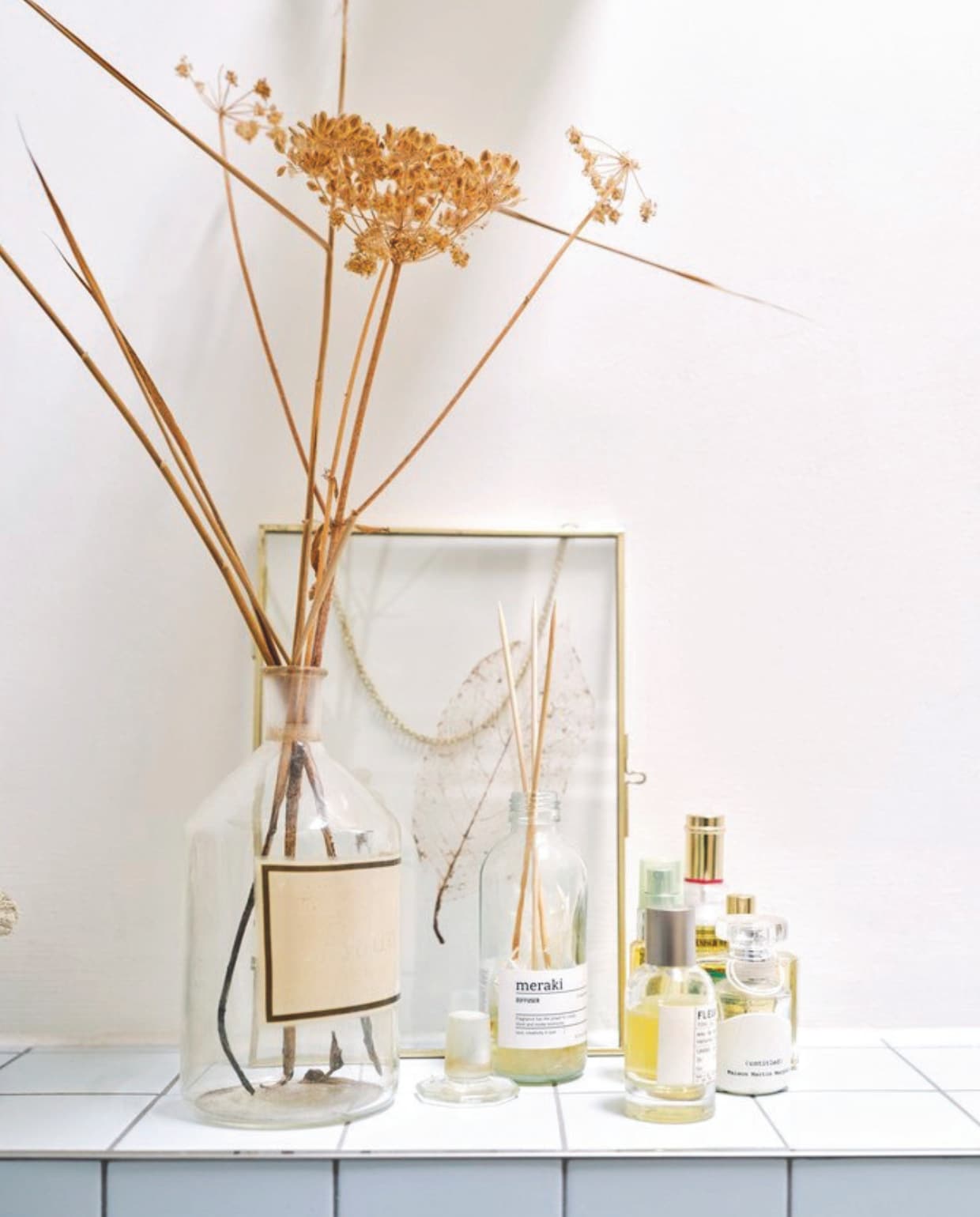 Oude laboratoriumfles met gedroogd fluitekruid, kringloop. Glazen lijst Xenos met gedroogde takjes van de Etna op Sicilië, geurstokjes Meraki, parfum Fleur d’oranger 27 van Le Labo. vtwonen 03-2025 | fotografie rené van der hulst | tekst merel van der lande