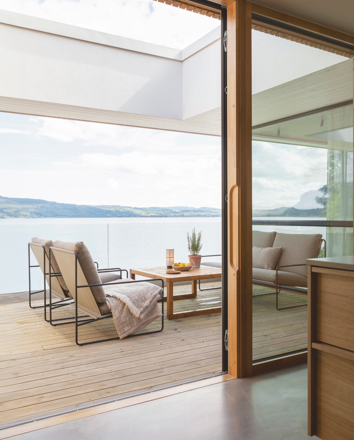 Op de veranda naast de keuken staan een buitenbank en stoelen van Ferm Living. Tafel Skeidar. Terrasvloer Møreroyal van Talgø. Stijlvol Wonen 03-2025 | Fotografie Anne Bråtveit | Tekst Caroline Westdijk