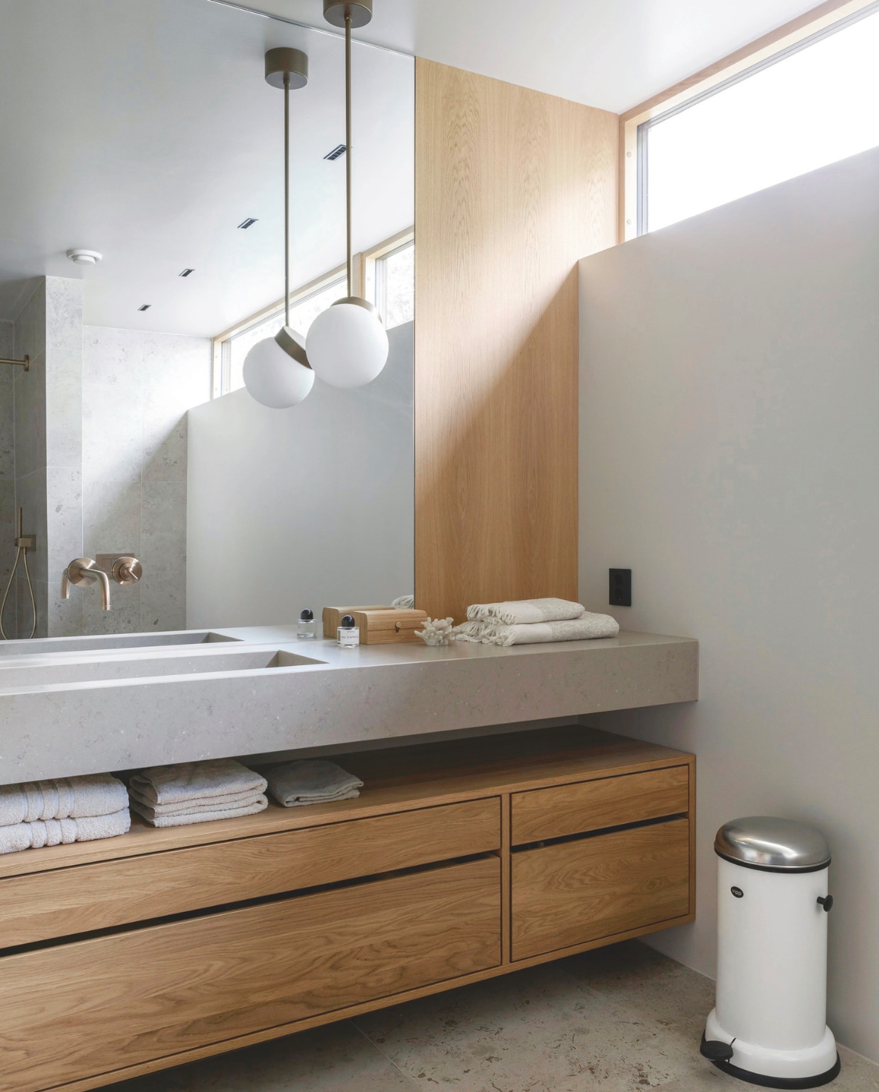 De badkamer is deels voorzien van eikenhouten wandpanelen. Het wastafelmeubel is maatwerk van Fjellby. Blad met geïntegreerde wastafel van Silestone van Cosentino, via Fossline. Kraan Axor. Lamp Polaris ZTR van Lucis. Handdoeken Høie. Vloertegels Modena. Stijlvol Wonen 03-2025 | Fotografie Anne Bråtveit | Tekst Caroline Westdijk