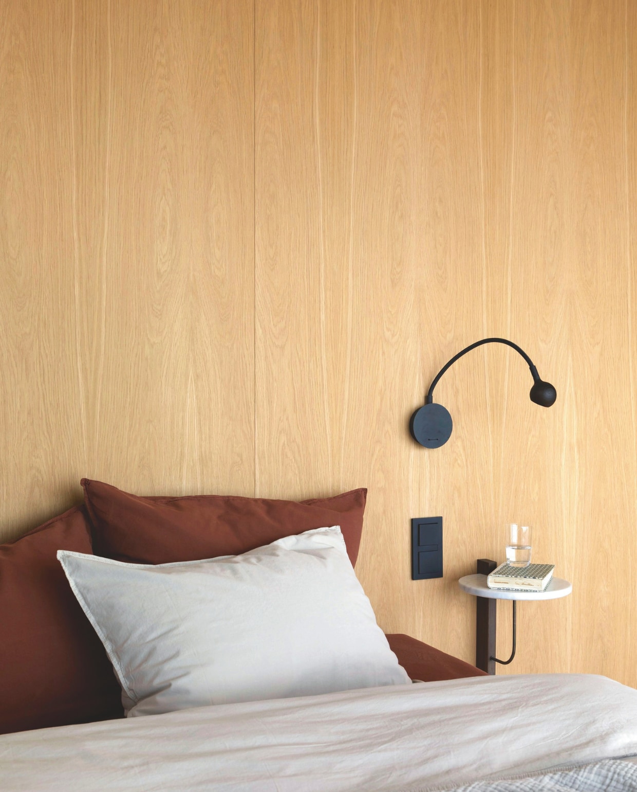 De muur achter het bed is van vloer tot plafond voorzien van eikenhouten panelen. Nachtkastje Audo Copenhagen. Leeslamp No8 van Marset. Beddengoed Høie. Stijlvol Wonen 03-2025 | Fotografie Anne Bråtveit | Tekst Caroline Westdijk