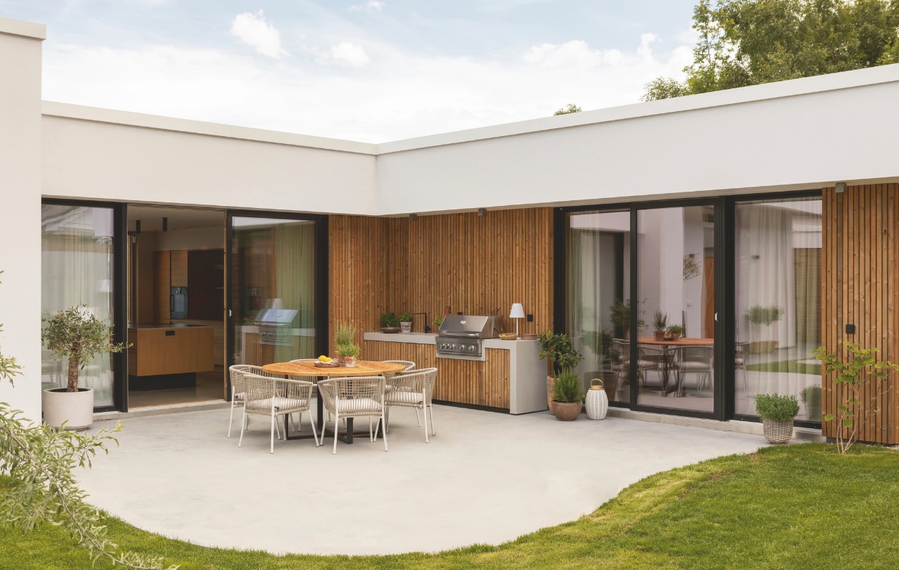 Het beton in de atriumtuin heeft een organische vorm die contrasteert met de rechte lijnen van de woning. De buitenkeuken is op maat gebouwd door Fjellby met een rvs inbouwbarbecue van Mustang Grill. Ettafel Slettvol. Stoelen Ikea. Stijlvol Wonen 03-2025 | Fotografie Anne Bråtveit | Tekst Caroline Westdijk