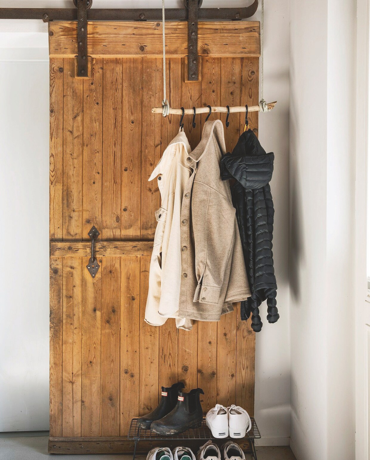 Hangende kapstok gemaakt door Anna-Lena van een tak en touw. Schuifdeur is een kaal gemaakte oude staldeur. Soortgelijke deuren Destijdsch. Schoenenrek Ikea. vtwonen Landelijk 03-2025 | Styling Miriam Hannemann | fotografie André Reuter | tekstbewerking Chris Muyres