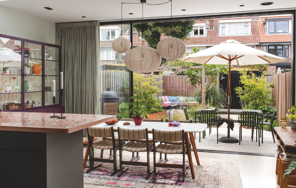 Tafel Wehkamp. Stoelen vintage. Kandelaar Hay. Bloempot Blokker. Metalen fruitmand Pt. Bollampen Zara Home. Kleed Living Maroc.  Kandelaars H&M Home. Paarse kast Oldwood. Bureau design van Joris Splinter. Krukken Ikea. Eettafel en -stoelen buiten Hay. Parasol Skagerak. Barbecue The Bastard. Gordijnen By Mölle. vtwonen 03-2025 | fotografie Studio Keeelly