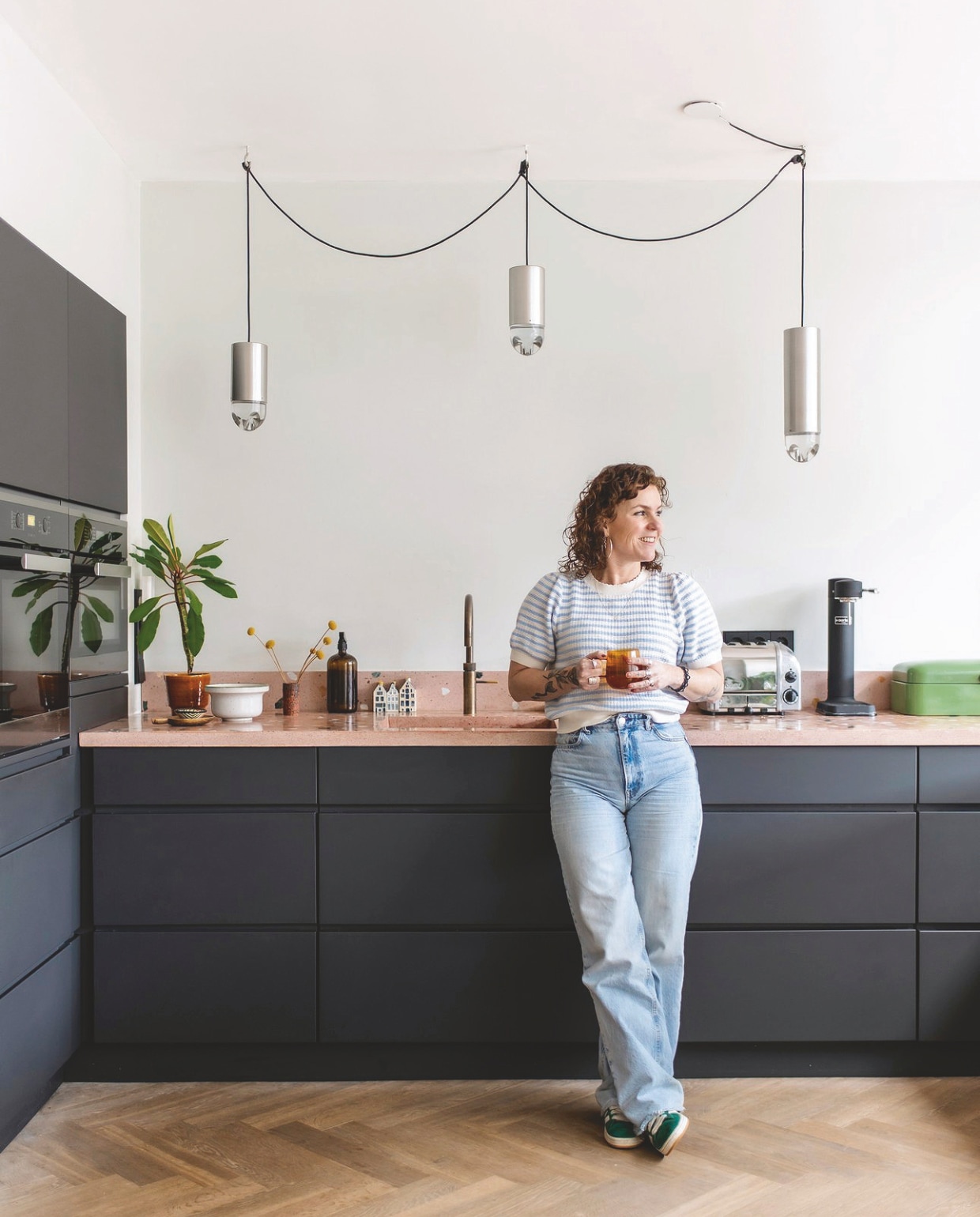 Keuken en nieuwe zwarte fronten Kvik. Keukenblad met spoelbak Pronck. Hanglampen Raak uit ouderlijk huis Jessica. Visgraatvloer Echt Parket. Broodtrommel, witte pot en vaas vintage. Muurverf Lab Wallpaint Classic Coral Vestingh. vtwonen 03-2025 | fotografie Studio Keeelly | tekst Caroline Westdijk