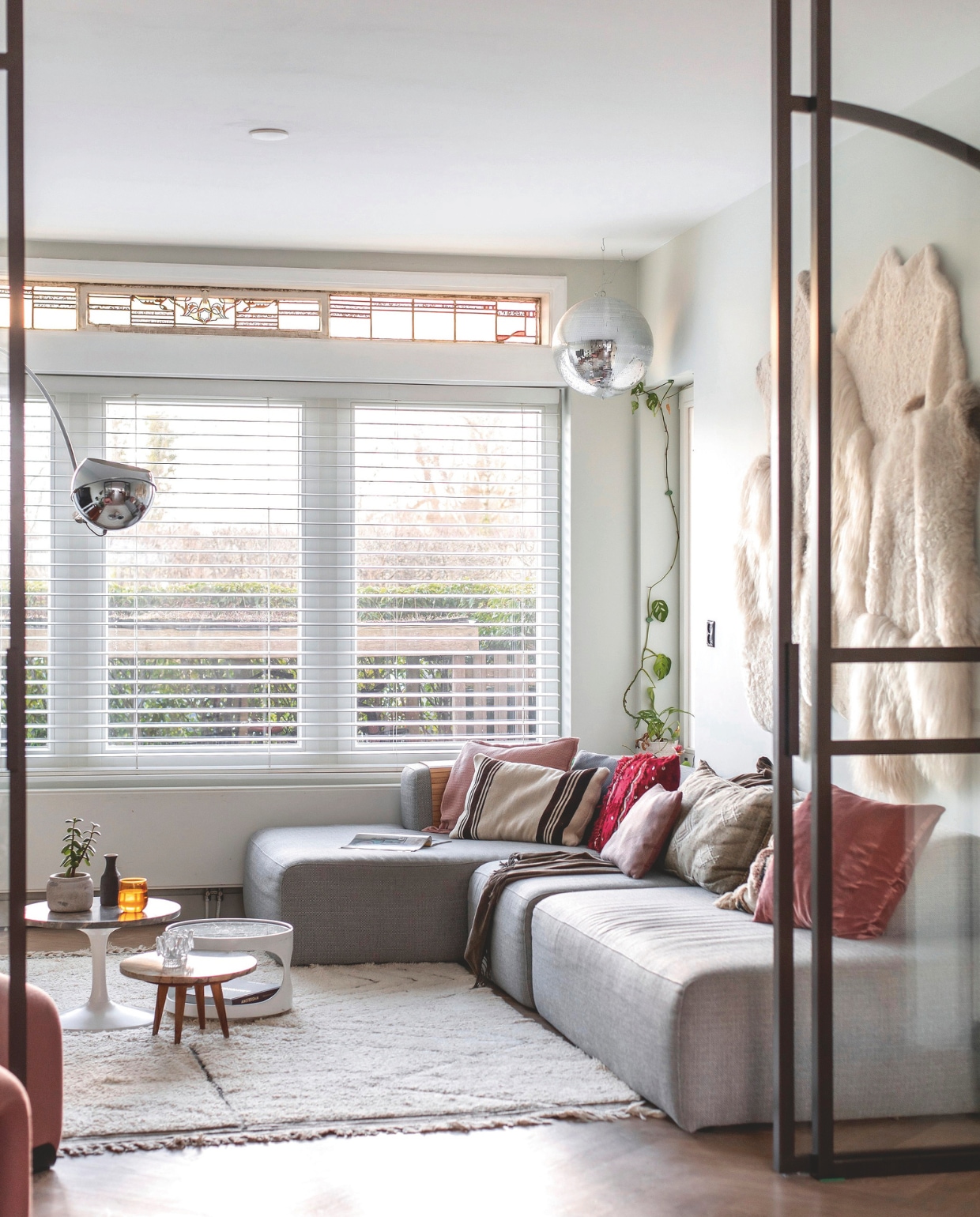 Bank X6 van 4x6 sofa. Kussens Karwei, Ikea, Hema en Stoov.  Vintage tafel met witte poot en houten bijzettafel Sip&Clara Pop-up Store. Witte bijzettafel met ronde opening en vaas vintage. Glas Sissy-Boy Homeland. Vloerkleed Living Maroc. Zilveren bollamp uit ouderlijk huis Jessica. Stalen schuifdeuren Stuimer Metalworks. Schapenvachtenkleed Van Buren Bolsward. vtwonen 03-2025 | fotografie Studio Keeelly | tekst Caroline Westdijk