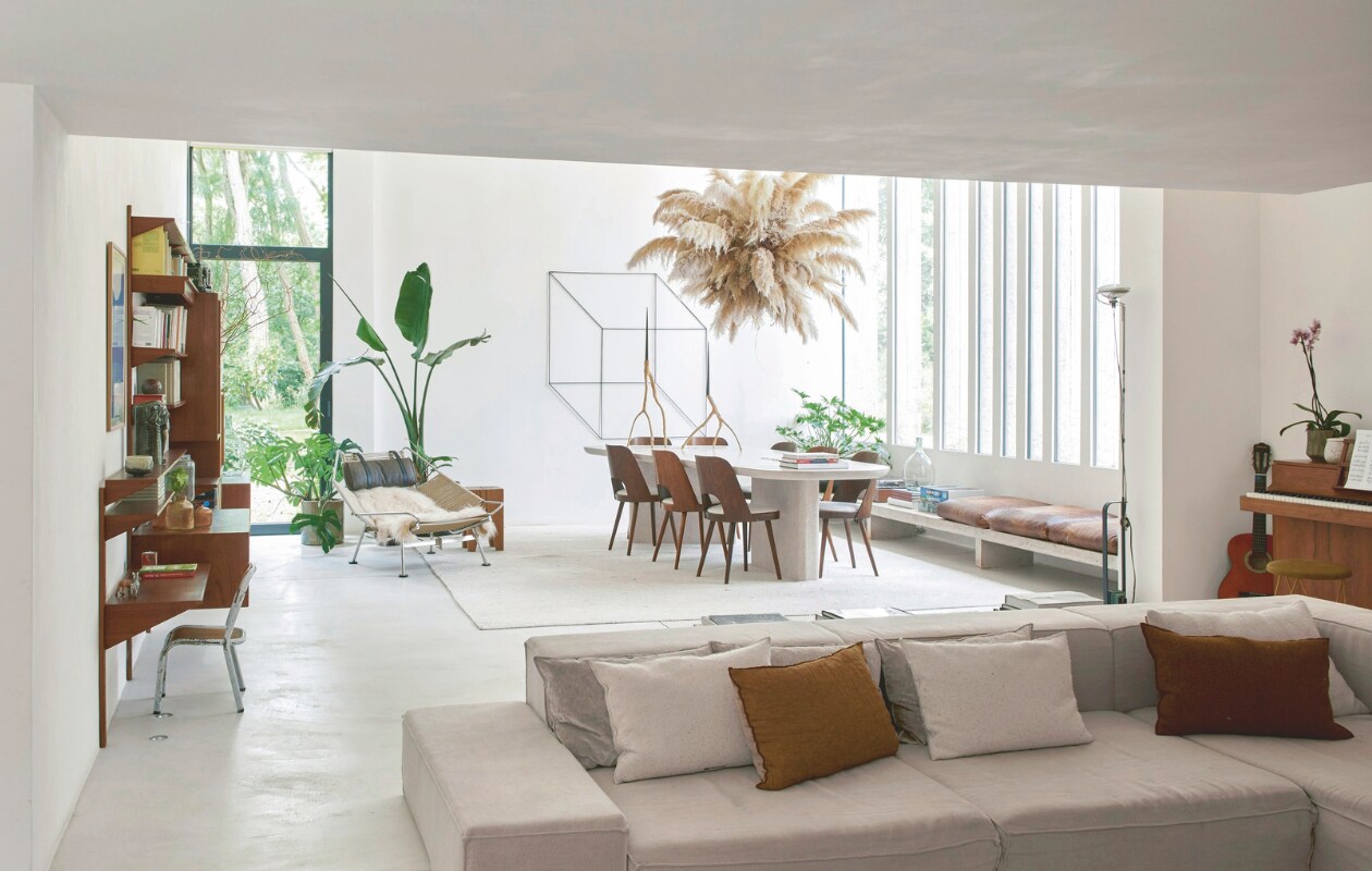 De zithoek loopt over in de eetkamer. De lage bank en de natuurstenen tafel zijn ontworpen door Catleen. ‘Ik ben een perfectionist. Daarom heb ik er lang over gedaan om de tafel vorm te geven.’ Bloeminstallatie van Horty Poetry, stoelen van architect Oswald Haerdtl. Kubusvormig kunstwerk van Antonio Sciortino. Loungestoel Flag Halyard van Hans Wegner. Wandmeubel en stoel links vintage. vtwonen stijlvol 03-2025 | Fotografie Mr. Frank |Tekst Tanne Donjacour Gielen