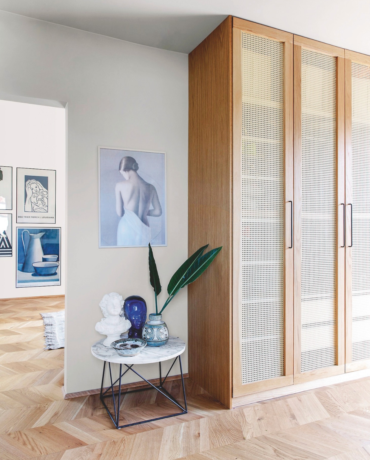 Kast Pax van Ikea, eikenhouten ombouw en deurframes met rotan op maat gemaakt. Marmeren tafel erfstuk. Poster van een straatartiest in Parijs. vtwonen 04-2025 | styling Rikke Graff Juel | fotografie Christina Kayser O.
