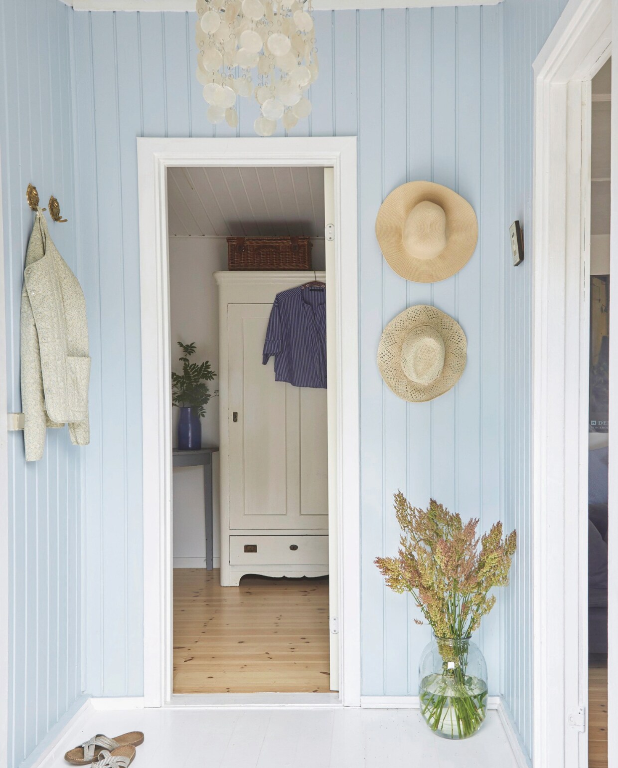 De houten vloer is wit geverfd. Het blauw van de muren mengde Gitte zelf. Rieten hoeden vintage. Soortgelijke lamp metparelmoer schelpen reliving.nl. Deense slippers Shangies bijvoorbeeld bij huushinne.nl. Kast erfstuk van Gittes grootouders. Vaas Tine K Home. vtwonen Landelijk 4-2025 | Styling Rikke Graff Juel | Fotografie Anitta Behrendt | Tekst Wilma Tjalsma-Smits