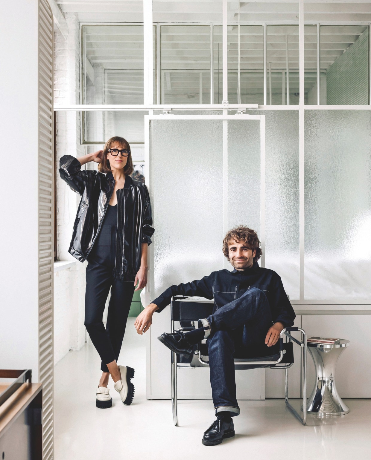 De matglazen wand naar het slaap- en badgedeelte in een idee van B-architecten, die de diamantslijperij verbouwden voordat Frédérique de loft kocht. Raphaël zit op een Knoll Wassily stoel van Marcel Breuer, daarnaast een limited edition Tam Tam kruk van Henry Massonnet. De witte rolkast is het model Pastoe A’dammer van Aldo van den Nieuwelaar. Stijlvol Wonen 05-2025 | fotografie Katoo Peeters | tekst Maya Toebat