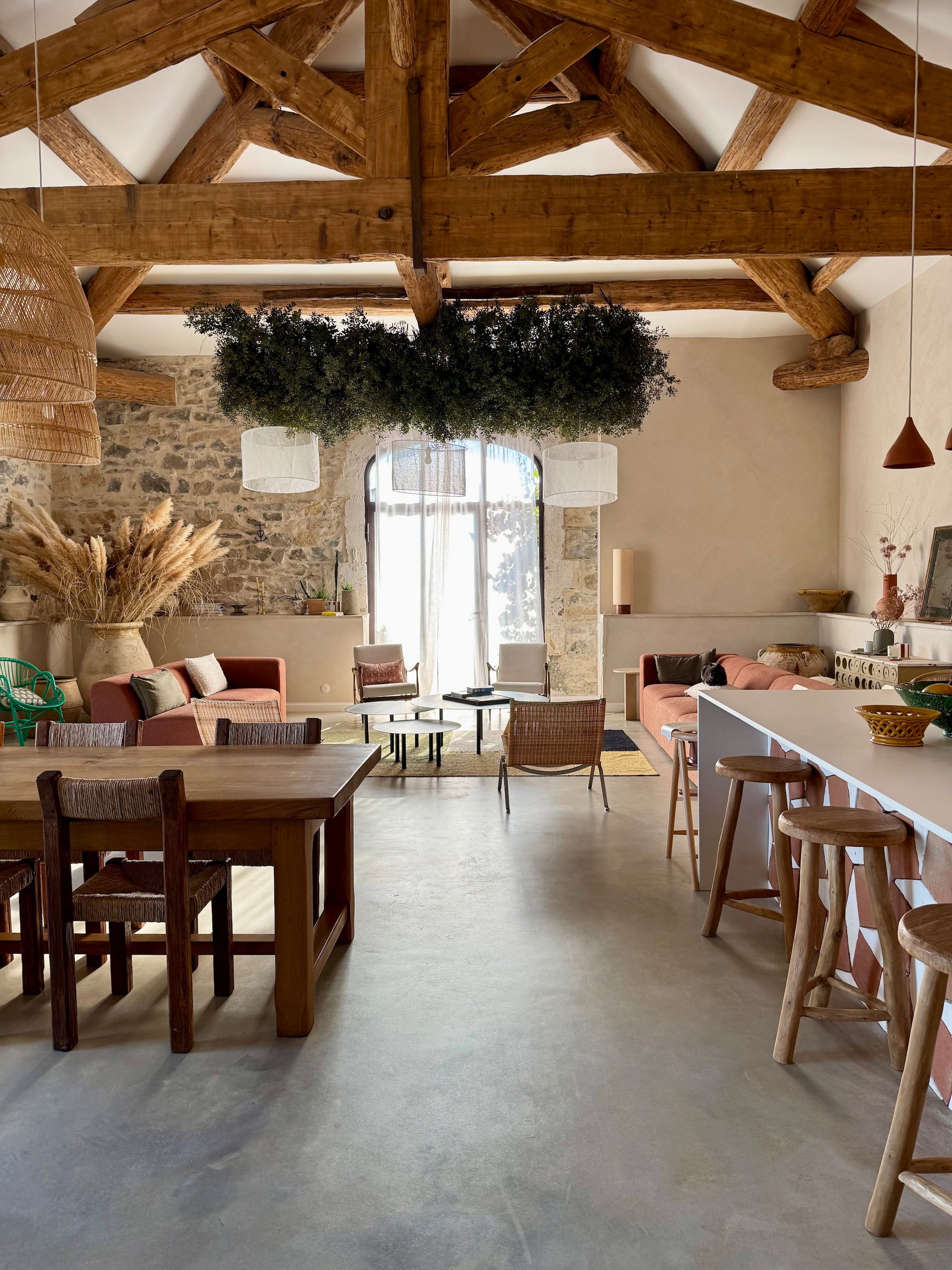 Keuken Ikea met op maat gemaakte fronten en matwit Dekton werkblad. Barkrukken La Madeleine Déco. Hanglampen La Maison Pernoise. Stoelen in Brutalist-stijl geweven door Arnaud, tafel kringloop. Rotan hanglampen My Bohem. Vloer gepolijst beton, muren geschilderd met kalkverf van Mercadier in kleur Boumian. Banken By Sidde, metalen salontafels zelfgemaakt, katoenen kleed Saudade Design. Fauteuil Rua Madeira, rotan stoelen PK22 van Poul Kjaerholm voor Fritz Hansen. Travertin bijzettafel Talka. Groene installatie gemaakt van schijnhulst. vtwonen 07-2025 | fotografie Manon Ferra