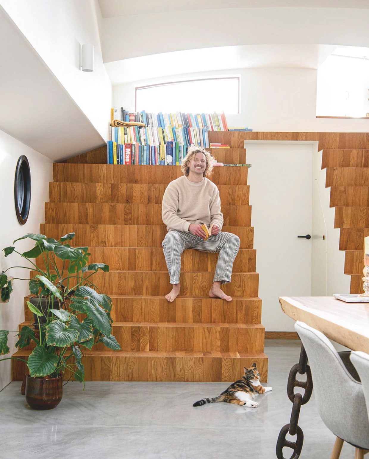 Jelle op trappen van Nederlands eikenhout. De trap rechts leidt naar het voorterras, de trap links leidt naar niks, maar is een speels visueel element en wordt gebruikt als boekenplank. vtwonen 05-2025 | styling Marit Saladini | fotografie Louis Lemaire | tekst Jackie Oomen