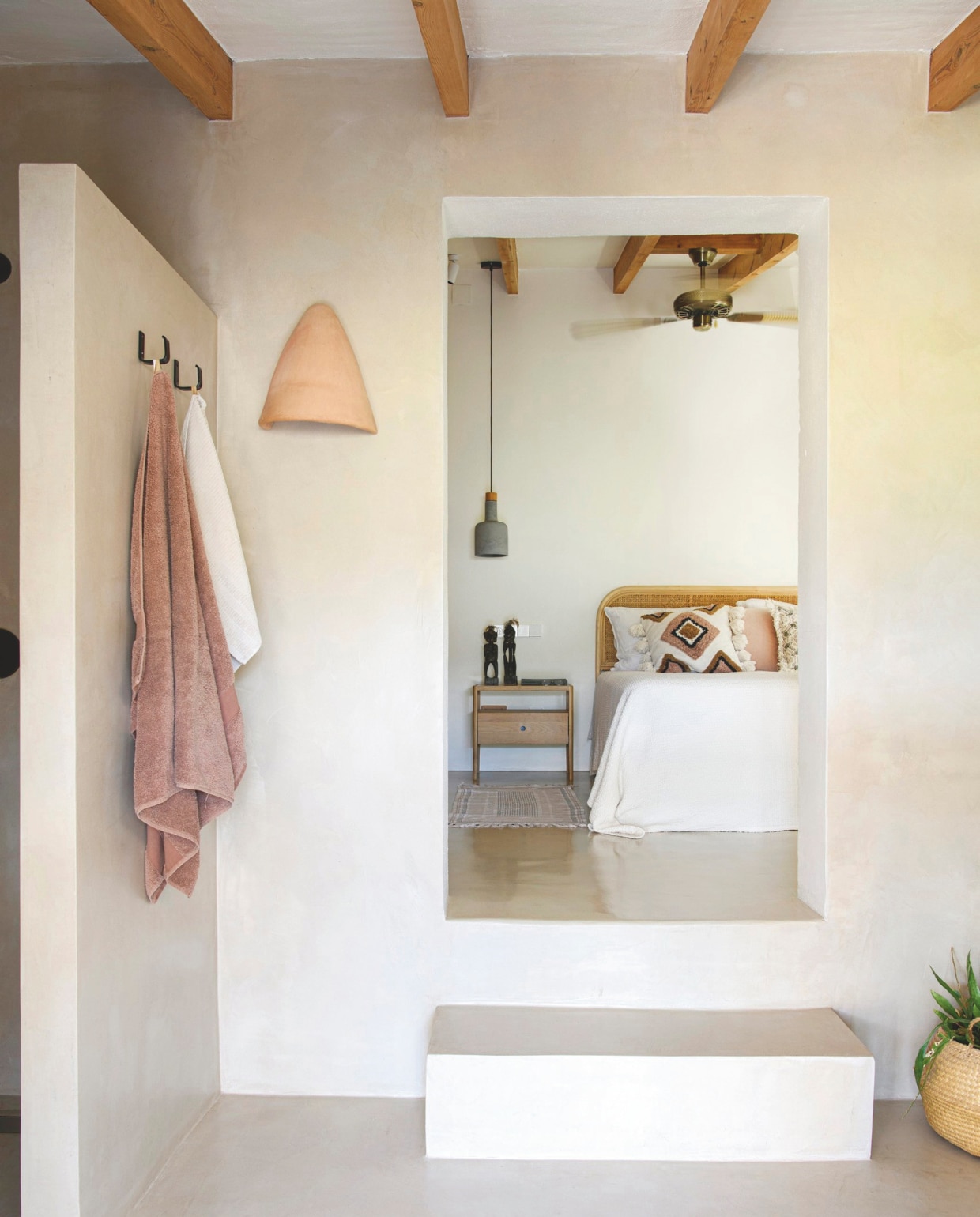 Bed lokaal beddenbedrijf. Kussens H&M Home. Nachtkastje Ethnicraft. Lampen Dutchbone. Mat, handdoeken en sprei Zara Home. Beelden souvenirs uit Afrika. Wandhaken op maat laten maken bij metaalbedrijf. Wandlamp van lokaal keramiekbedrijf. vtwonen zomerboek 2025 | styling Inge van Lieshout | fotografie Louis Lemaire