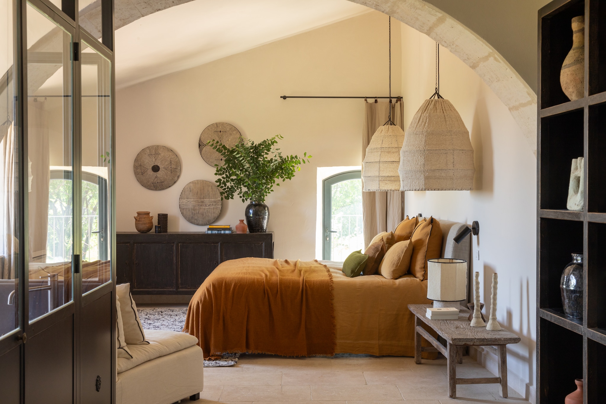 Op de wanden geborstelde kalkverf Tollens in Banc de roche. Bank en hanglampen Afghan Atmosphère d’Ailleurs. Sprei envintage linnen hoofdbord Maison de Vacances. Linnen gordijnen La Redoute. Roede Leroy Merlin. Leeslampen Creative Cables. Berber schilden La Maison Pernoise. Sidetable en Chinese vaas Versmissen. Vloerkleed Menorca van Idaho. Bedlinnen Couleur Chanvre. Kussens Casamance en Maison de Vacances. vtwonen Landelijk 07-2025 | styling Marie-Maud Levron | fotografie Cécile Perrinet Lhermitte  | productie Anne Catherine Scoffoni