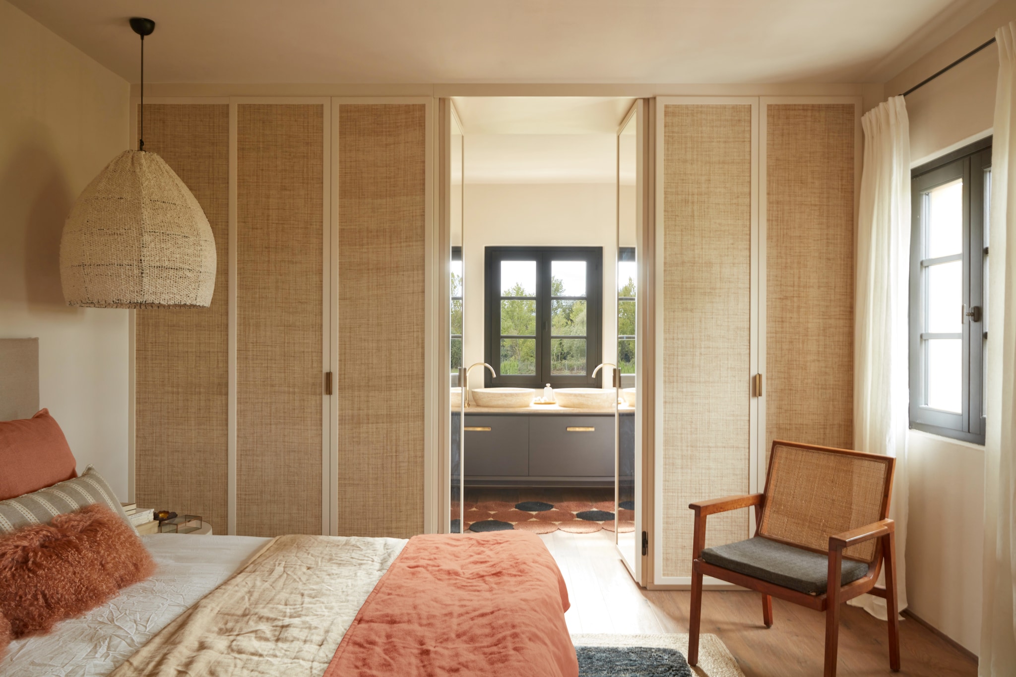 In deze slaapkamer komen ambacht en textuur samen: een Afghaanse hanglamp van ruwe katoen (Atmosphère d’Ailleurs), linnen gordijnen van Paolo Nesi, een kledingkast van hout met webbing van plantvezel. Vergelijkbare kasten via La Redoute. vtwonen Landelijk 07-2025 | fotografie Gaelle Le Boulicaut