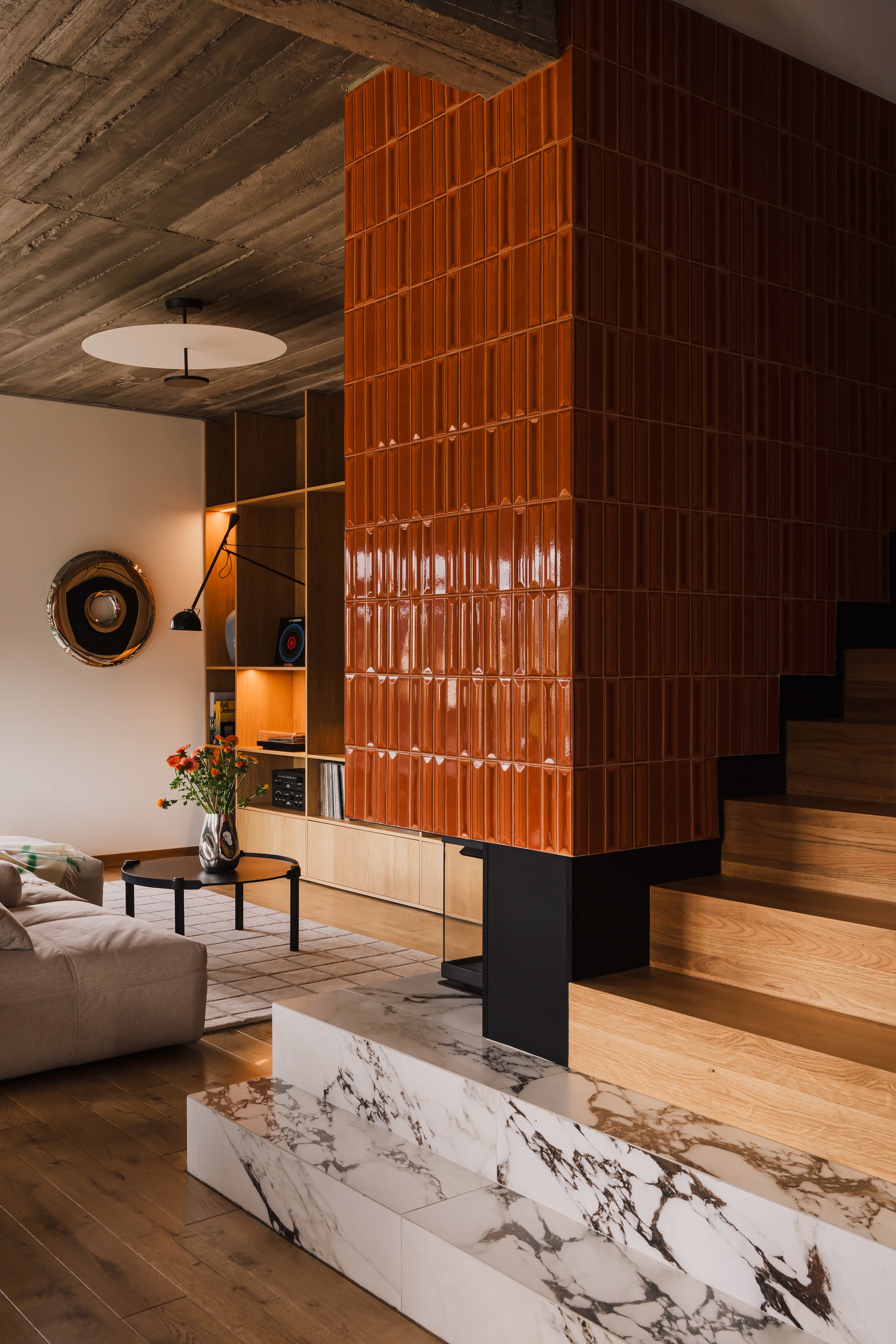 De woonkamer met plafondlamp uit de FLAT-collectie, ontworpen door Ichiro Iwasaki voor Vibia. Rondo 95 Mirror van Zięta. Vaas Mirror van Westwing Collection. De haard met structuurtegels uit de Flauti-collectie van Ceramica Vogue. stijlvol wonen 7-2025 | productie Kubieniec + Dlugosz | fotografie Zasoby Studio
