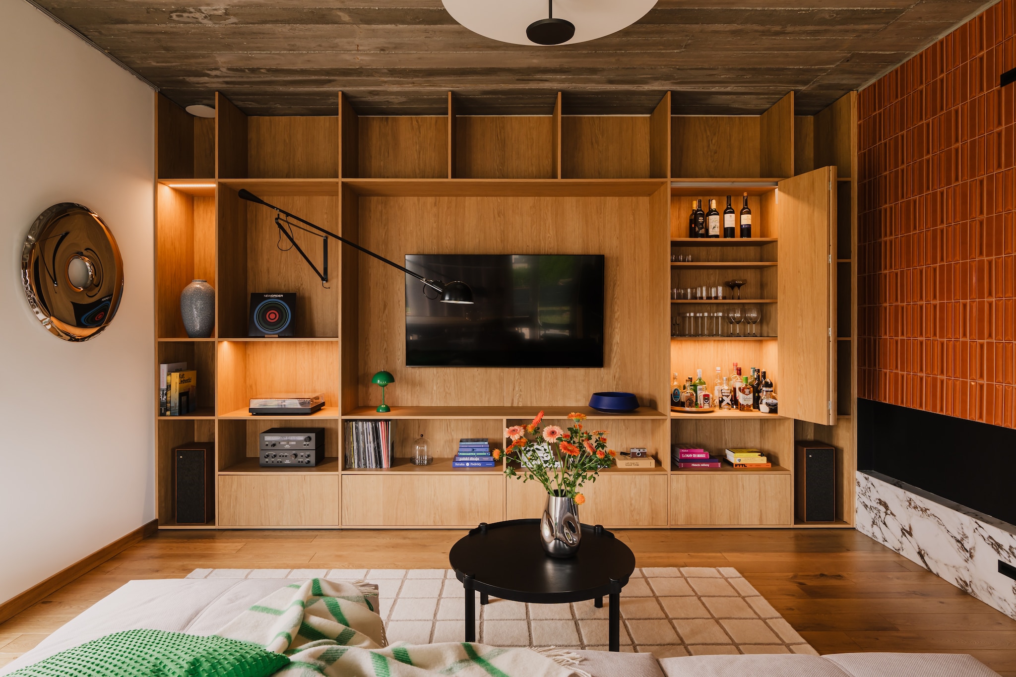 Het wandmeubel in ere hersteld: de op maat gemaakte houten tv-kast dient meteen als bar en audiohoek. Zwenkbare wandlamp 265 van Paolo Rizzatto voor Flos. Tafellamp Flowerpot VP9 van &Tradition. stijlvol wonen 7-2025 | productie Kubieniec + Dlugosz | fotografie Zasoby Studio