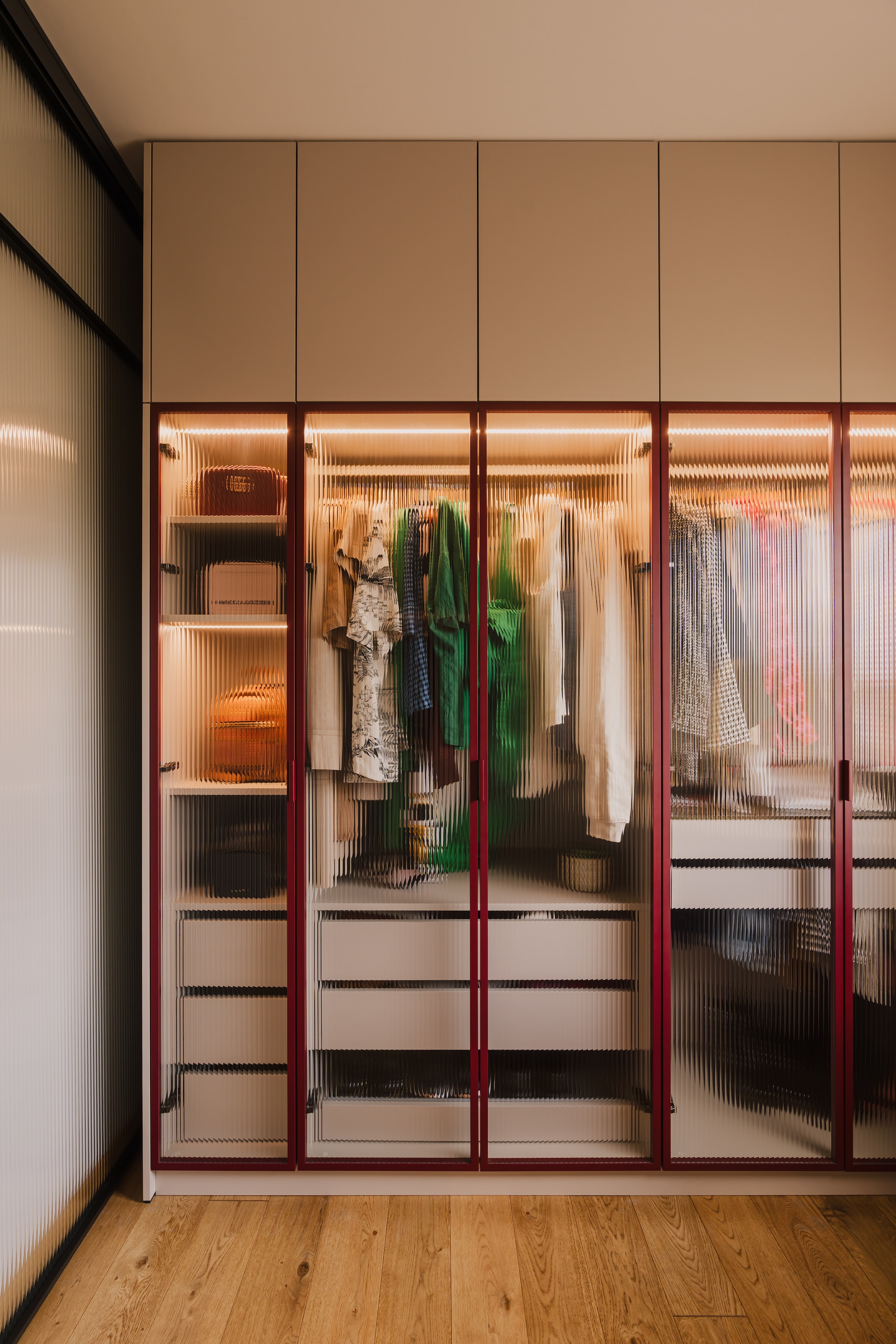 Alle meubels in de inloopkast, inclusief de bordeauxrode ladekast, zijn door een timmerman speciaal voor deze ruimte op maat gemaakt. Tafellamp Luminous Circle van HK Living. RECHTS: Garderobekast met ribbelglas, via glas.nl. stijlvol wonen 7-2025 | productie Kubieniec + Dlugosz | fotografie Zasoby Studio