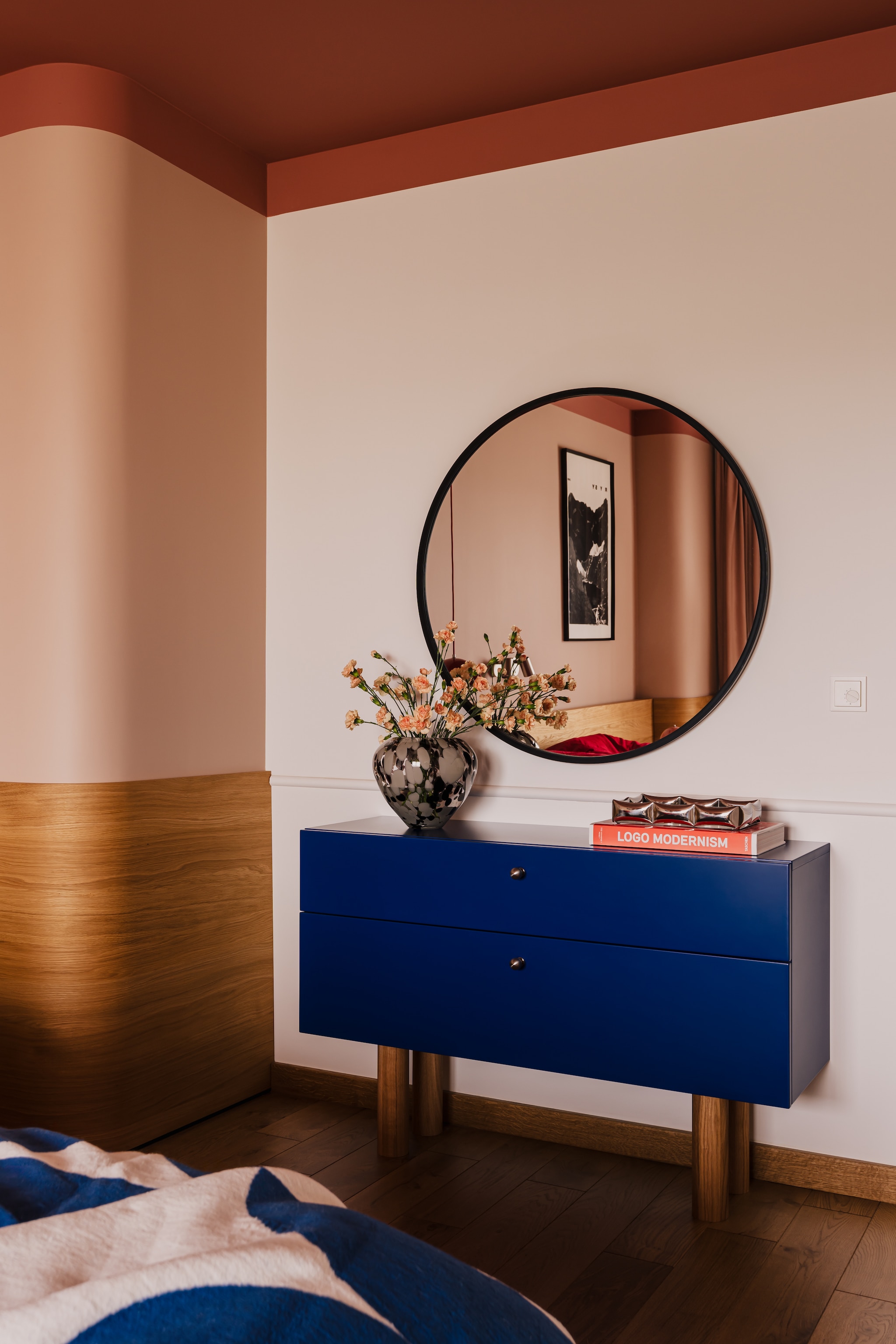 De slaapkamer met gebogen houten lambrisering en sfeervol terra plafond. Het blauwe dressoir is speciaal ontworpen om te harmoniëren met andere blauwe accenten in het interieur.  stijlvol wonen 7-2025 | productie Kubieniec + Dlugosz | fotografie Zasoby Studio