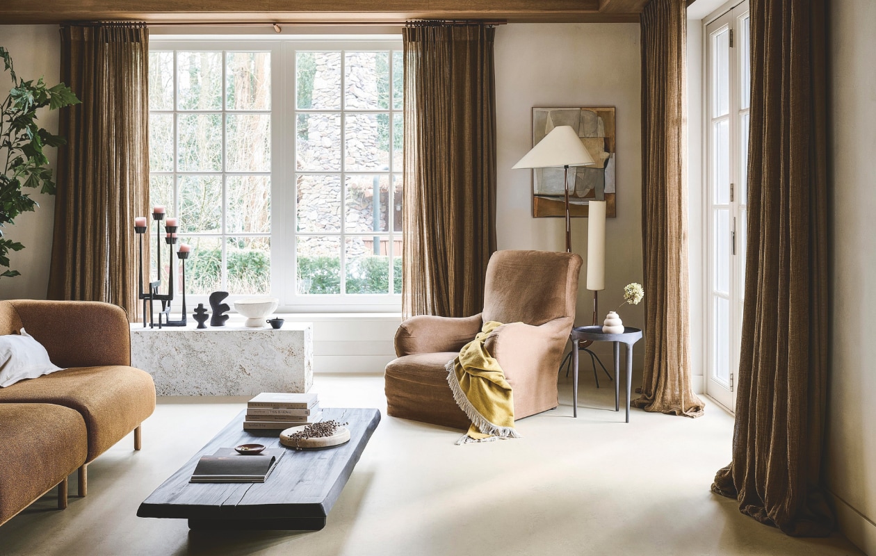 vtwonen Marmoleum vloer AlmondMarble, 200 cm breed, per m² € 52,40.M.m.v. demachinekamer.nl (bank), cassina.com (fauteuil), wdstck.eu (salontafel), 101cph.com (bijzettafel), zarahome.com (witte schaal, kussenhoes, travertin schaal, zwart potje, bruin schaaltje), woood.nl (kandelaar), fermliving.com (zwarte organische vazen), ilsevanstoltz.com (wandkunstwerk Naive). Overig privébezit. vtwonen Landelijk 05-2025 | styling Kim van Rossenberg | fotografie Sjoerd Eickmans