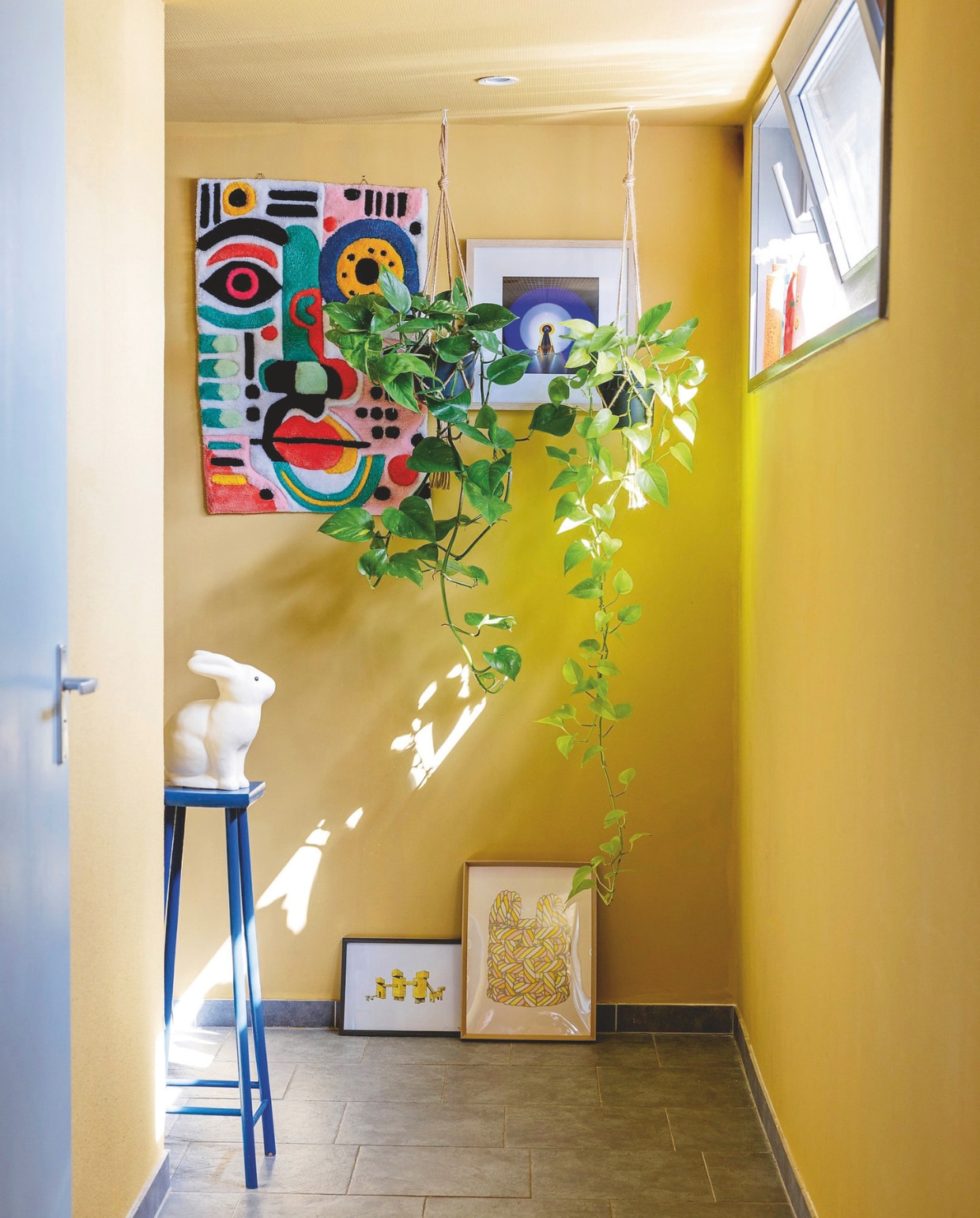 Muurverf Sudbury Yellow en Parma Grey van Farrow & Ball. Kruk Reliving. Konijn vintage. Wandtapijt Etsy. Kunstprints Museum Boijmans van Beuningen. Plantenhangers Intratuin. vtwonen 05-2025 | styling Ilona Jongepier | fotografie Dana van Leeuwen