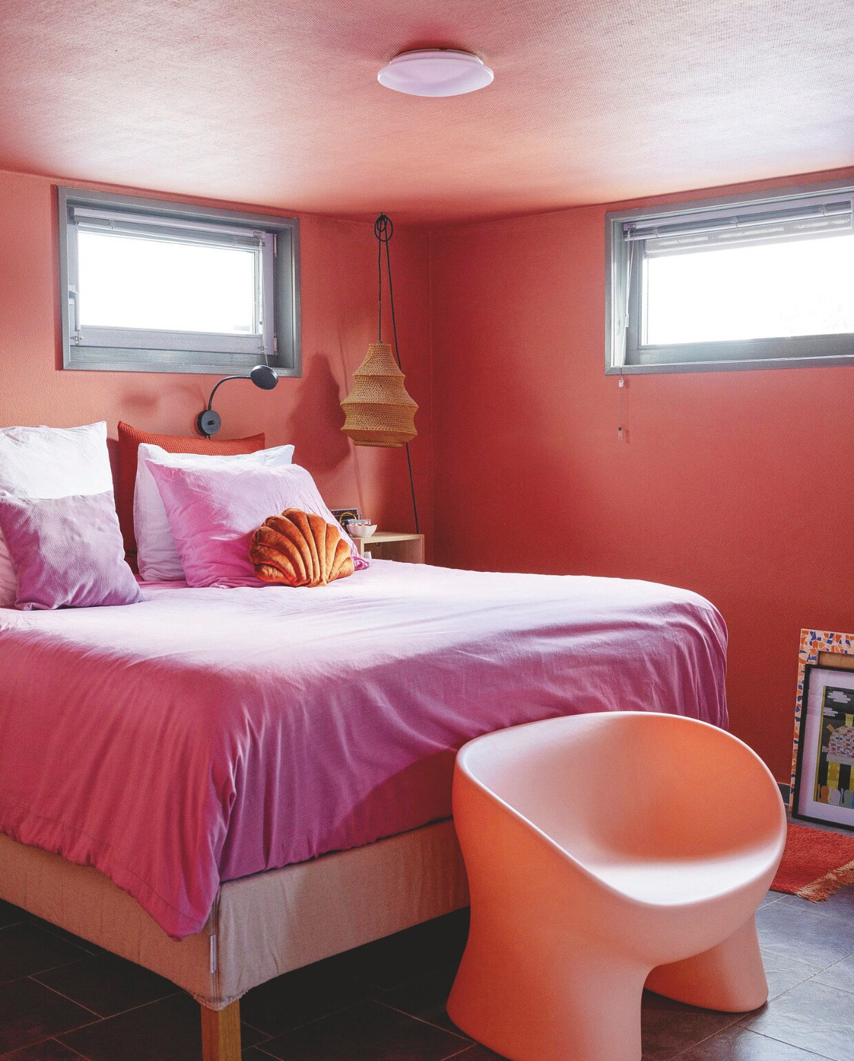 Muurverf Red Earth van Farrow &amp; Ball. Bed Ikea. Roze dekbed Wehkamp. Bank, hanglamp, schelpkussen, oranje vloerkleed Kwantum. Wandlamp Karwei. Nachtkastje Ikea. Schilderijen uit kringloopwinkels. vtwonen 05-2025 | styling Ilona Jongepier | fotografie Dana van Leeuwen | tekst Chris Muyres