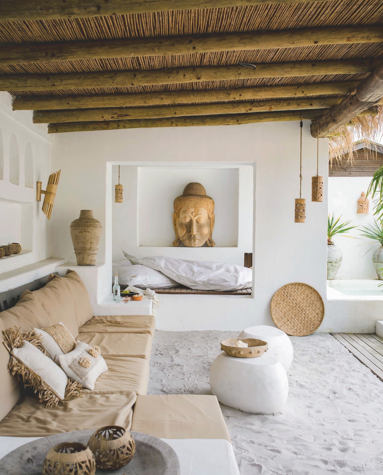 Loungebank zelfgemaakt door Arthur. Kussenhoezen maatwerk. Massiefhouten witte bijzettafels, Kelana terracotta schaal, linnen sierkussens, bamboe wandlamp, rotan schaal, windlichtjes, houten schaal, hanglampen, handgemaakt Boeddha-beeld en grote witte kussens Coco homeliving. vtwonen special zomerboek 12-2025 | fotografie Corine Hoge Bavel-Jansen | tekst Caroline Westdijk