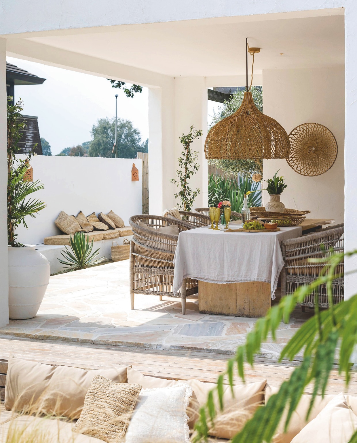 Eettafel, rotan stoelen, rotan open bloemlamp, diverse manden en schalen, rotan wandschaal Saringan, vaas Legian white, kussens op de voorgrond Coco homeliving. Tafelkleed Lovely Linen. vtwonen special zomerboek 12-2025 | fotografie Corine Hoge Bavel-Jansen | tekst Caroline Westdijk