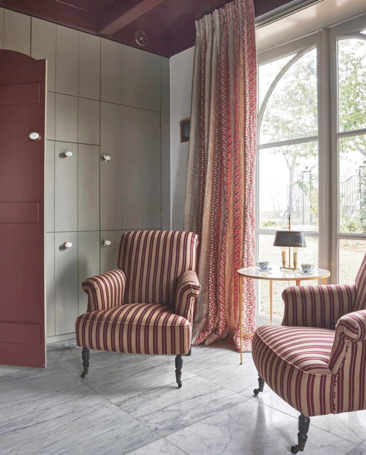 Fauteuil Bonifacio in stof Rayure Gladstone Nobilis, via Wilhelmine van Aerssen Agenturen. Bijzettafel Vaughan Designs. Antieke Bouillot tafellamp. Kastenwand op maat gemaakt door Hans Tinga. Kleur houtwerk Persiaans rood vanVettewinkel.