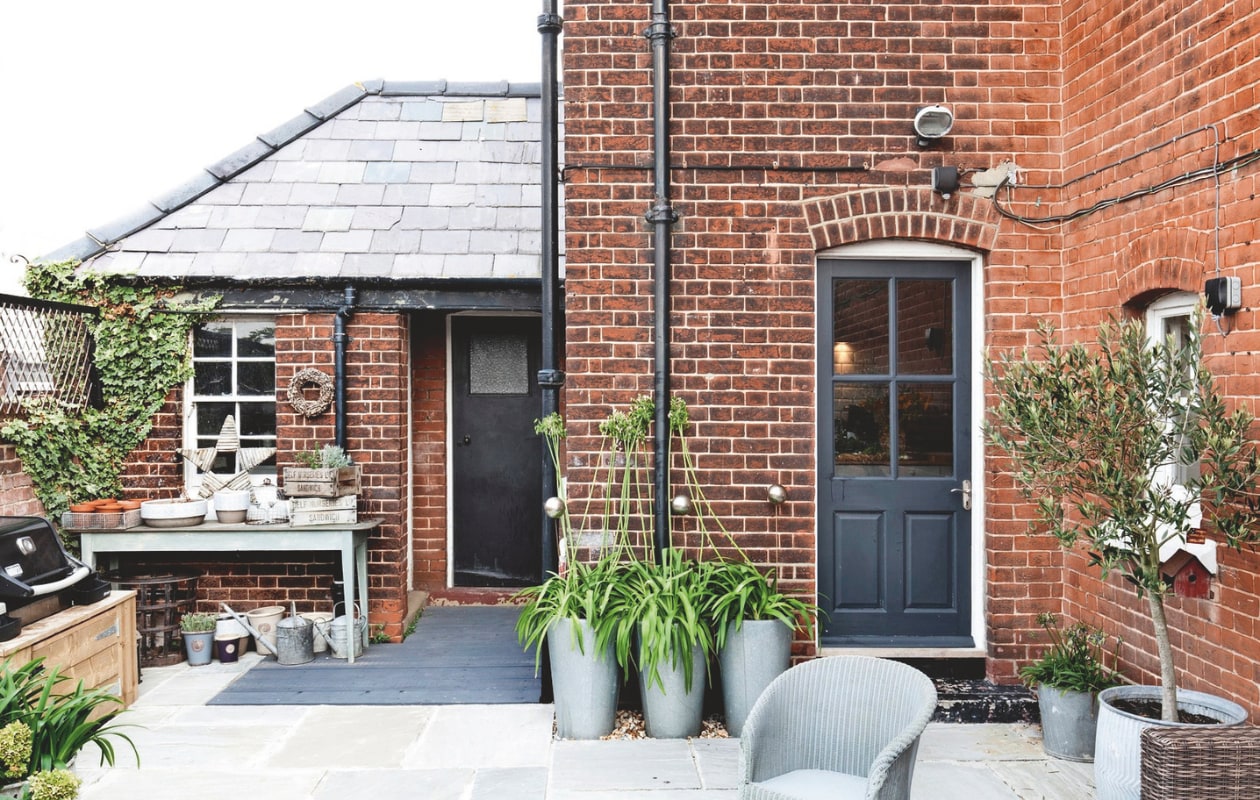 Zinken potten beplant met Agapanthus (Afrikaanse lelie). Achterdeur geverfd in Railings van Farrow &amp; Ball. Vintage tuinstoel Lloyd Loom. vtwonen Landelijk 04-2025 | styling Miriam Hannemann | fotografie André Reuter