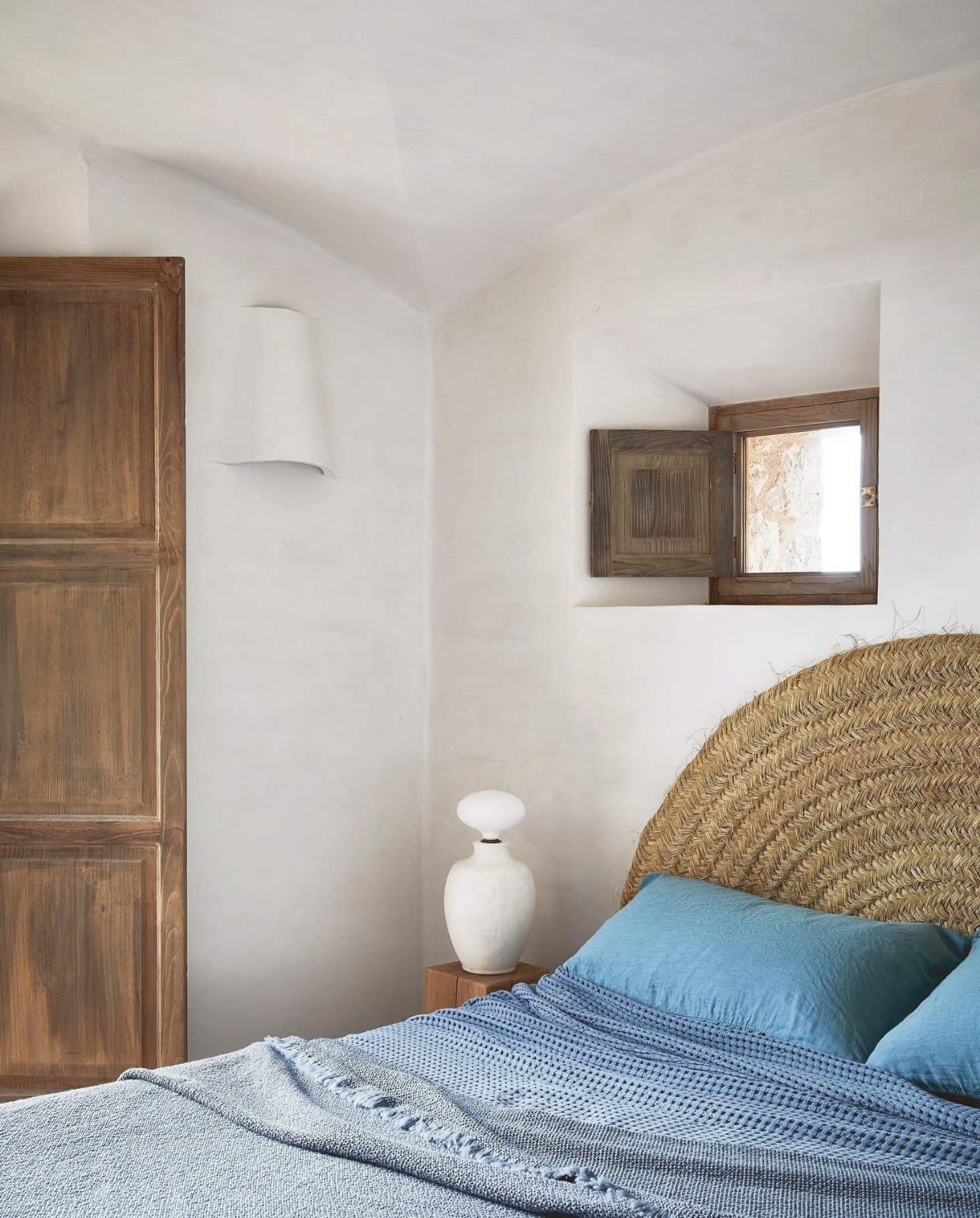 Een kleine slaapkamer op de benedenverdieping. Een ronde geweven grasmat, gekocht op een lokale markt, doet dienst als hoofdeinde. Wandlamp ontworpen door More Design. Nachtlamp uit de Mineral-collectie van More Decor. Beddengoed Society Limonta en uit de collectie van More Decor. Stijlvol Wonen 04-2025 | fotografie Greg Cox | tekstbewerking Anneleen Peeters | productie Sven Alberding/Bureaux/Living Inside | brontekst Robyn ALexander