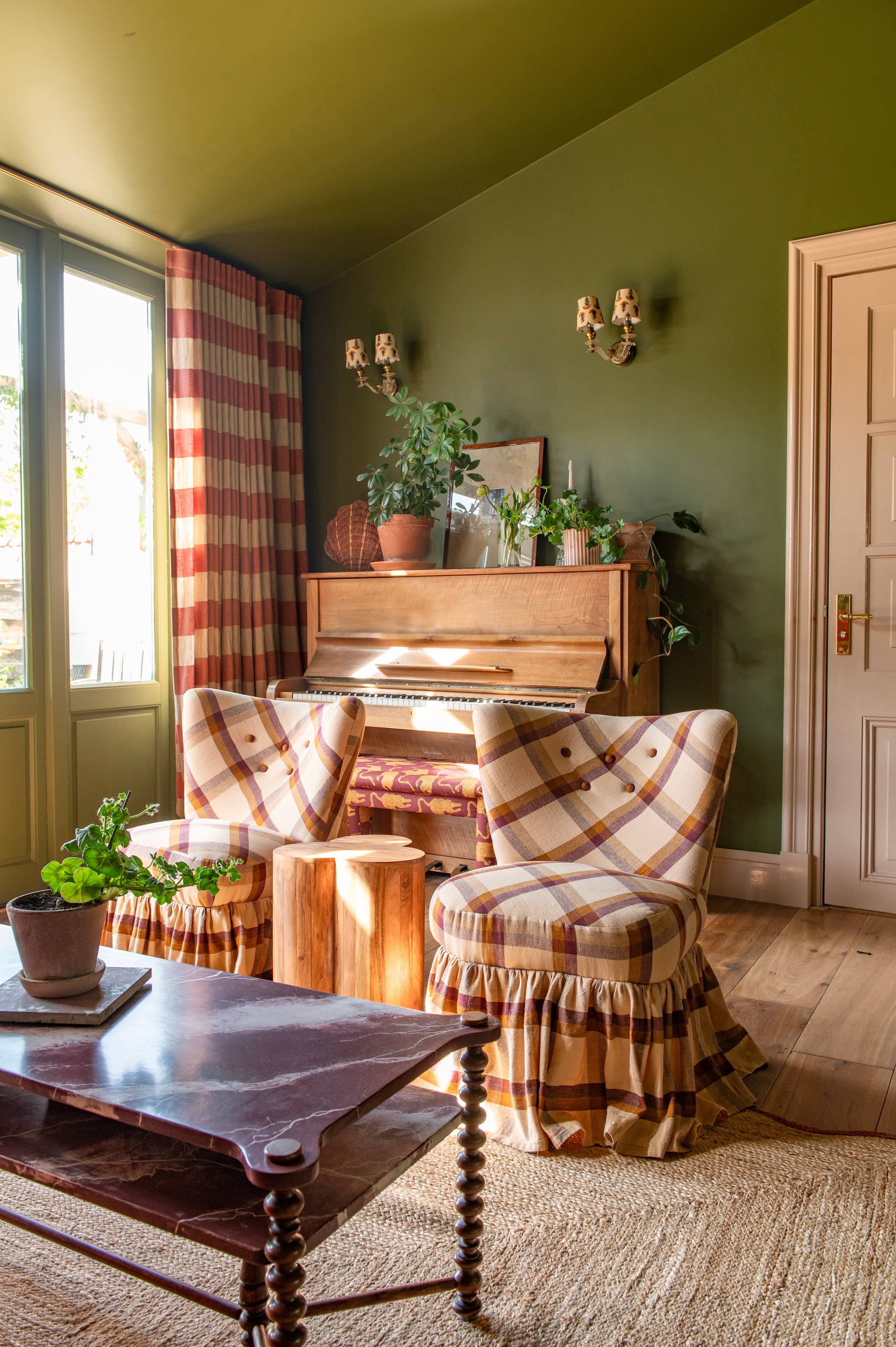Muurkleur Bancha van Farrow & Ball. Piano gratis opgehaald via Marktplaats. Gordijnen gemaakt met linnen stof van Bemz, wandlampen gevonden op antiekmarkt, kapjes van CheLuz. Pianokruk zelfgemaakt en bekleed met blockprint plaid van Doing Goods. Rieten schelp kringloop. Lijst met passe-partout via Passe-partout shop. vtwonen DIY special 03-2025 | fotografie Caroline Coehorst
