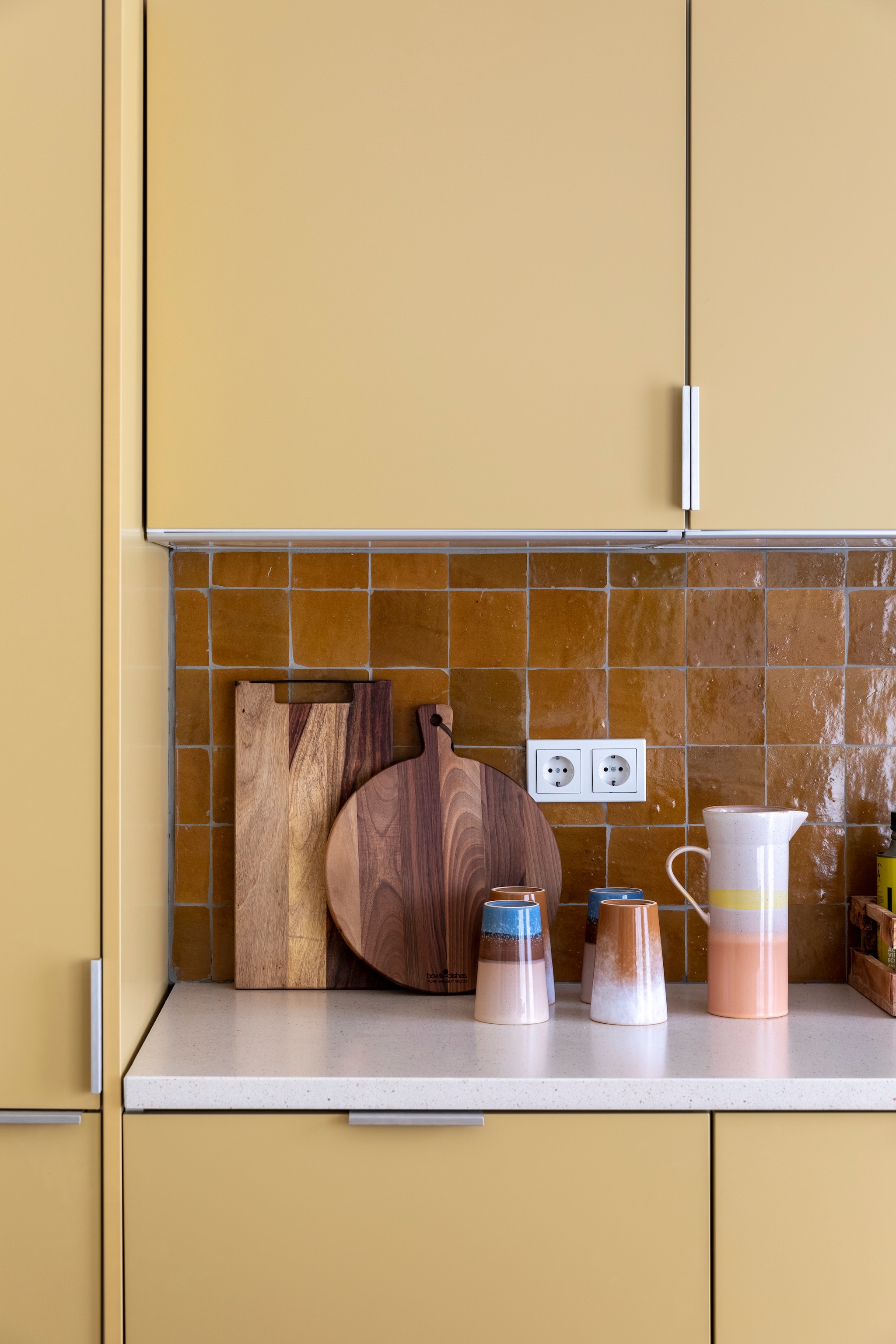 Flexa Creations muurverf om raam Midden Zandstrand (flexa.nl). Keuken op maat gemaakt (k14.nl). Tegels achterwand Zelliges Mustard, per m² € 114,95 (householdhardware.nl). Houten planken van Bowls en Dishes vanaf € 15,-, koraalkleurige kandelaar van À la € 30,-, gele kandelaar Flare van Hay € 49,-, groene glazen vaas van Bloomingville € 38,90 (vtwonen.nl). Vijzel € 28,44 (bowls-dishes.nl). Kan € 29,95 en theemokken € 11,40 van HKliving (eijerkamp.nl). Kunstwerk Neutrale collage van Laura Horn € 50,- (werkaandemuur.nl). vtwonen weer verliefd op je huis extra seizoen 15, aflevering 3 | styling Marianne Luning | fotografie Margriet Hoekstra