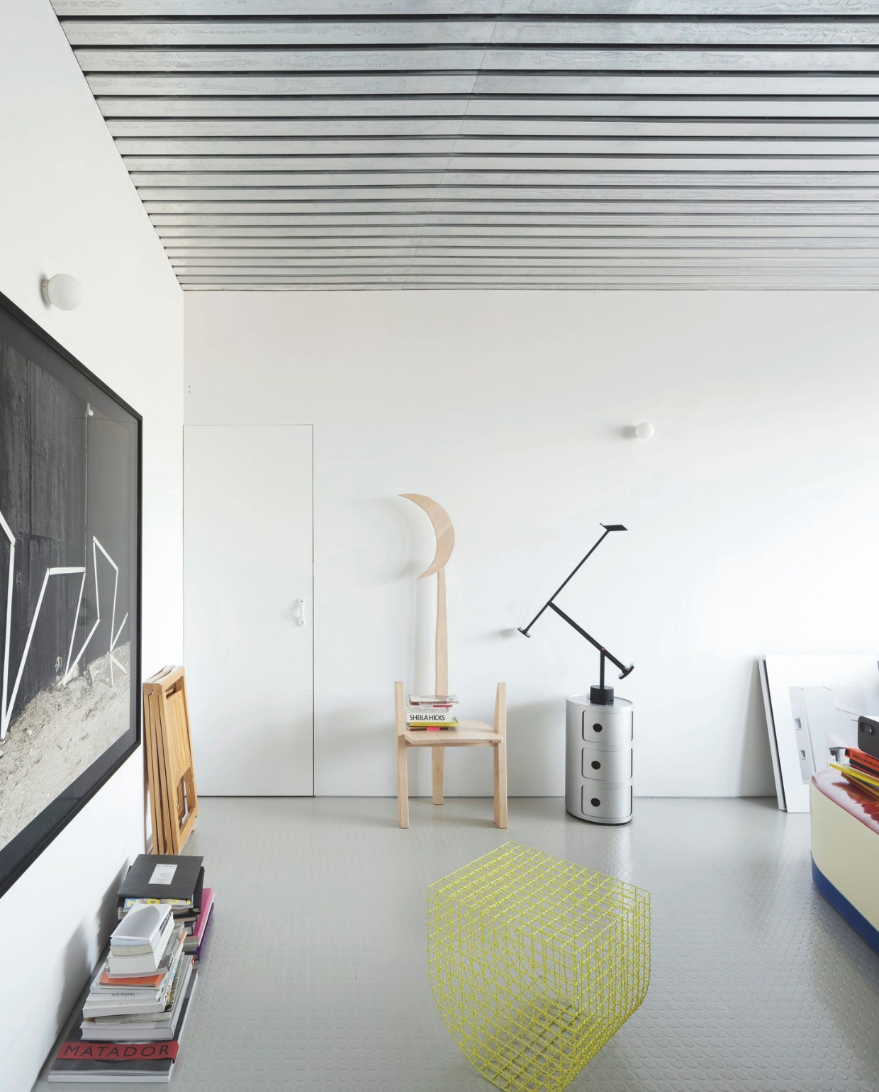 Een gegalvaniseerd stalen plafond en rubberen vloer reflecteren het licht en laten de ruimte groter lijken. Een mooie basis voor een designcollectie. Moon Chair van Casa Antillón. Klapstoelen Trieste van Aldo Jacober. Zwart-wit kunstwerk aan de muur van Nicolás Combarro. Zilverkleurige Componibili-kast van Kartell. Lamp Tizio van Artemide. Gele kruk van Tornasol. Stijlvol Wonen 05-2025 | fotografie Luis Díaz Díaz | tekst Jackie Oomen