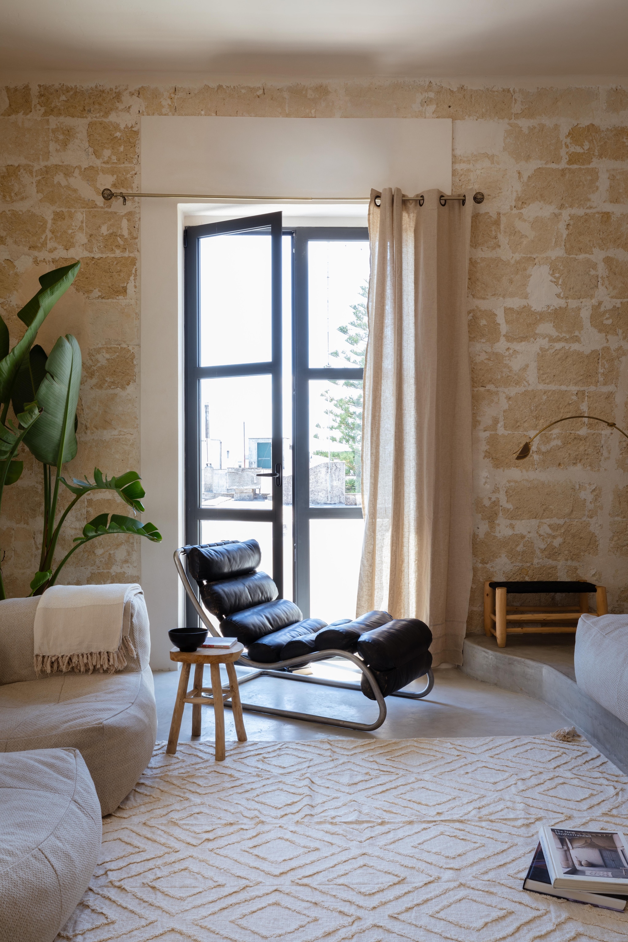 Vintage ottoman chair uit Nice. Mangohouten dressoir Sklum. Linnen zitmeubels en poef Olenka Interiors. Vloerkleed uit Marrakesh. Rattan spiegel Isidore van Tikamoon. vtwonen 08-2025 | productie Living Inside | fotografie Monica Spezia