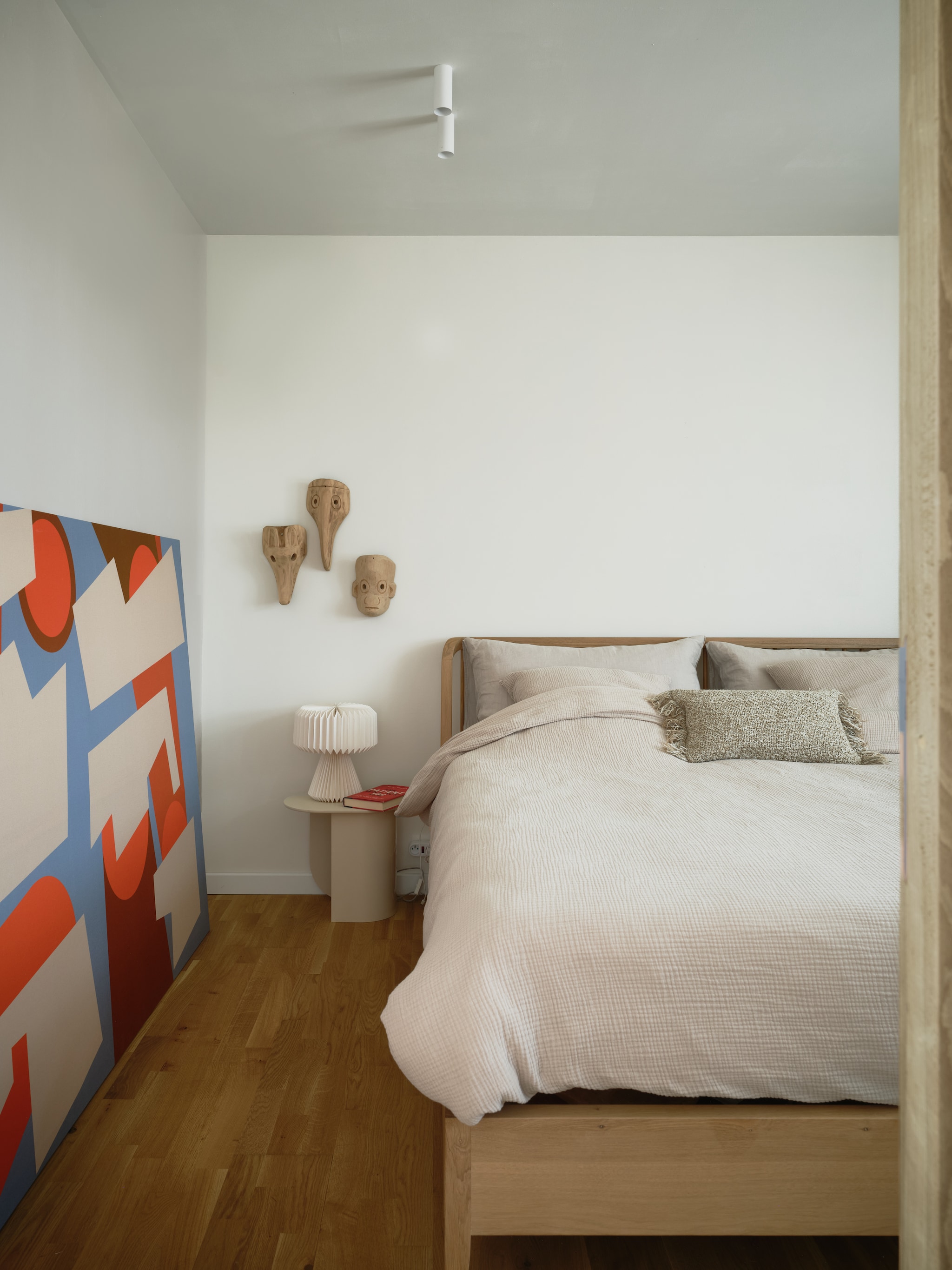 Bed Spindle van Ethnicraft. Nachtkastje Fést.Kunstwerk van Gregory B Studio. Maskers souvenirs uit Guatemala. Beddengoed H&M Home. Spots op maat gemaakt door Cone Lighting. stijlvol wonen 7-2025 | fotografie Mr. Frank